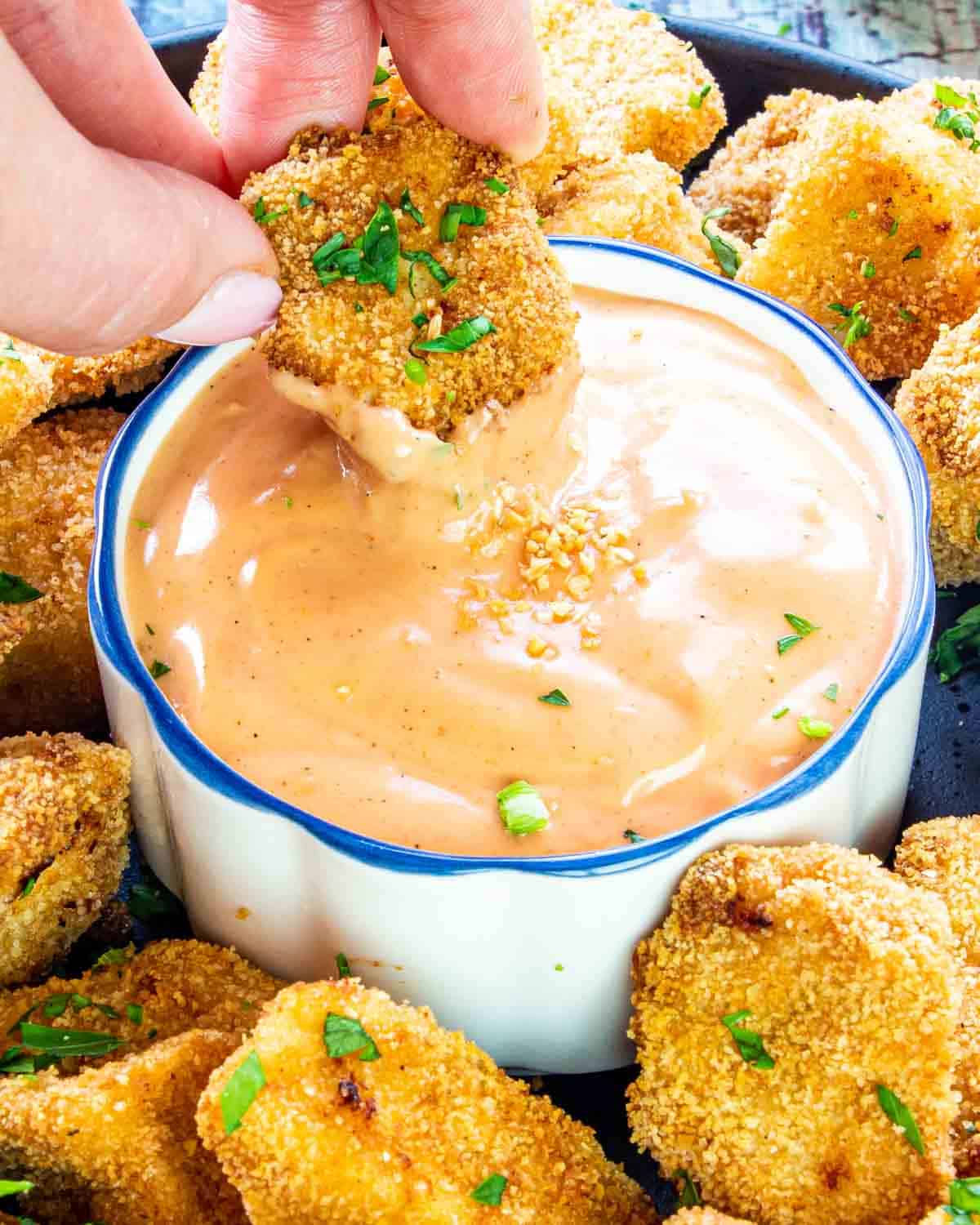 a hand dipping a chicken nugget in a bowl with fry sauce.