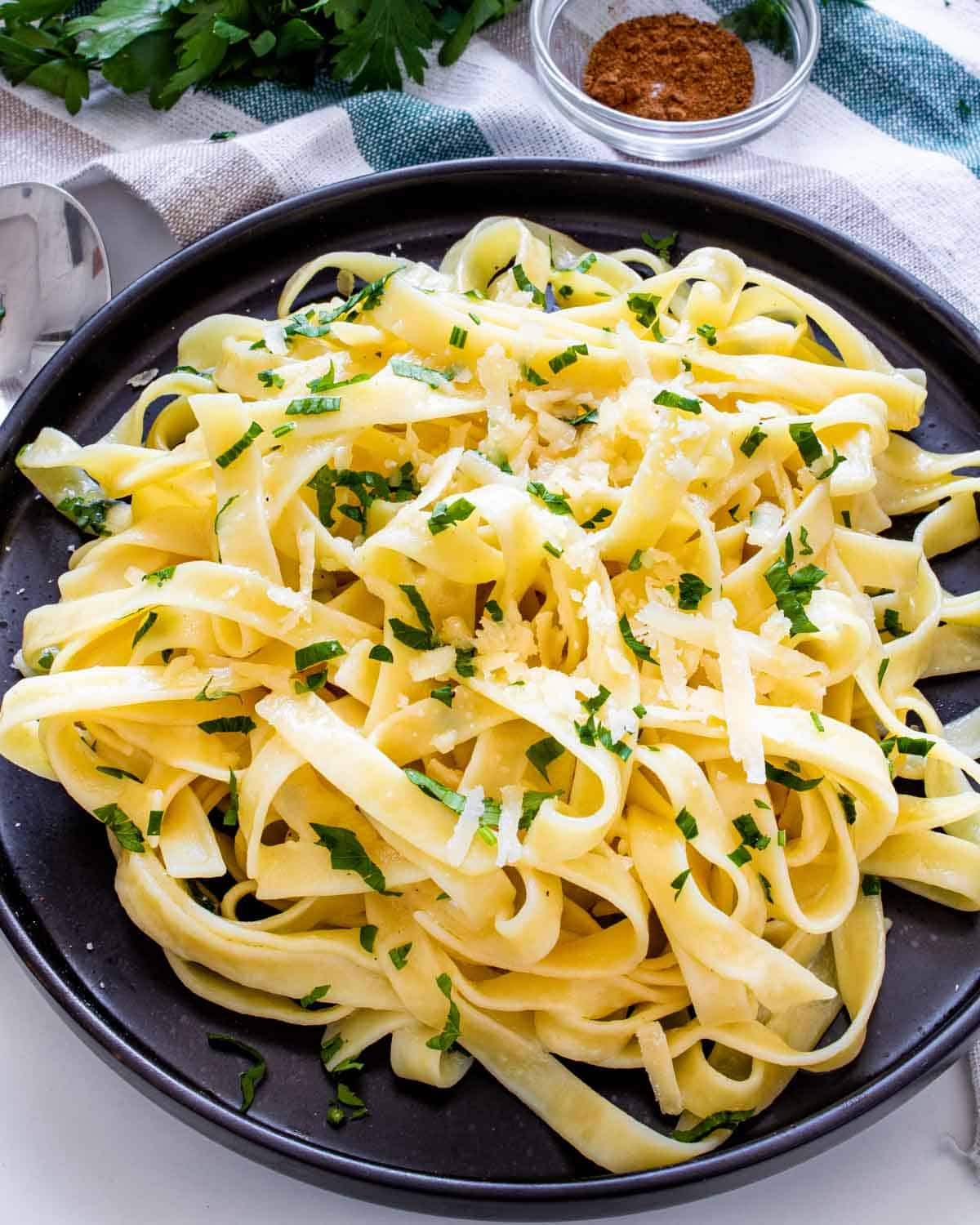 buttered noodles garnished with parsley on a black plate.