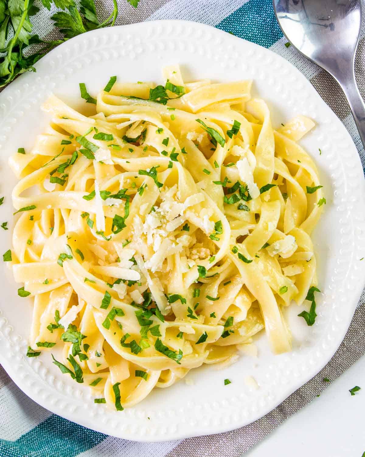 buttered noodles garnished with parsley on a white plate.