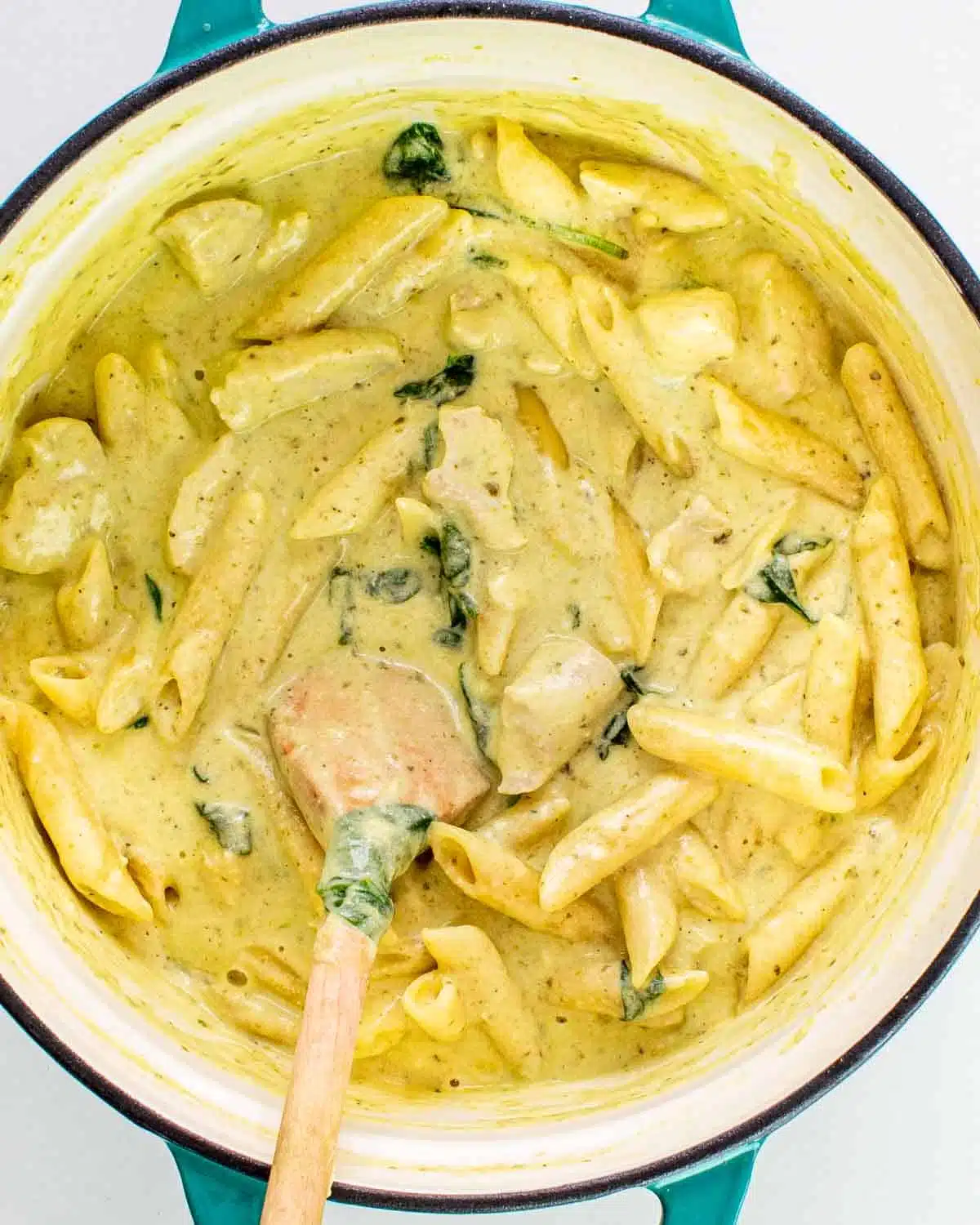 freshly made creamy pesto chicken pasta in a dutch oven with a wooden spoon inside.