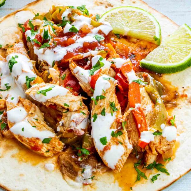 chicken fajitas on a tortilla garnished with sour cream and limes.