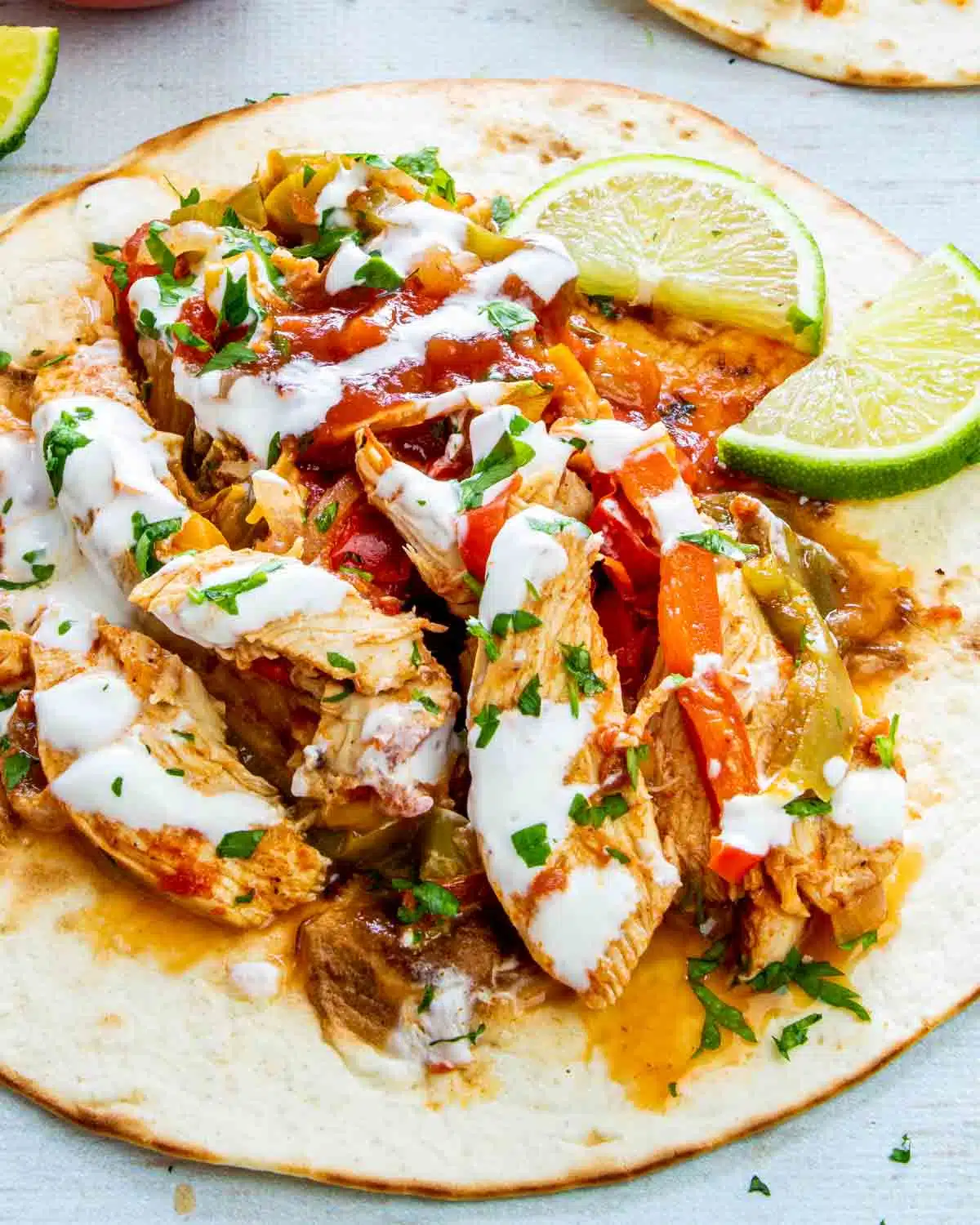 chicken fajitas on a tortilla garnished with sour cream and limes.