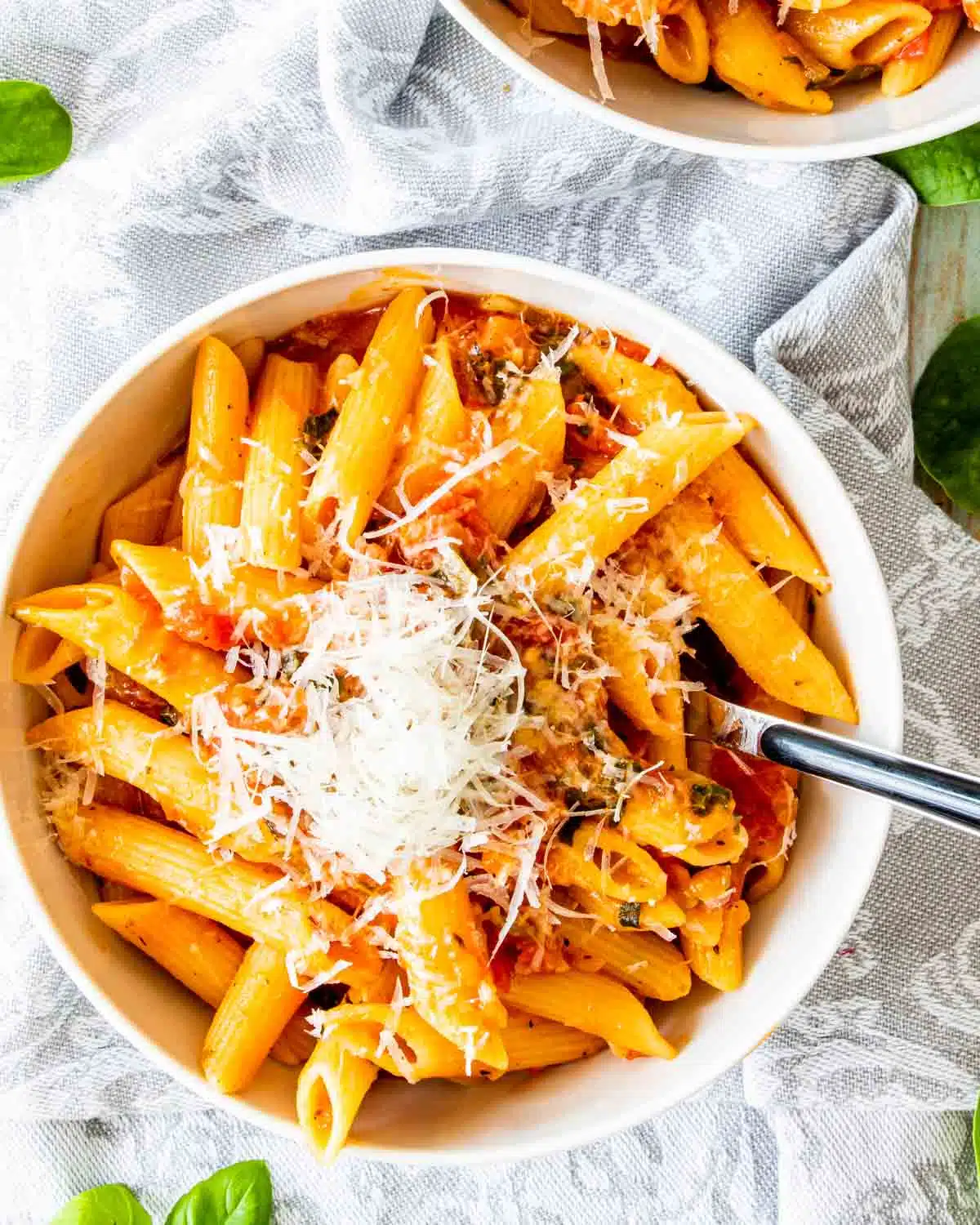 a serving of tomato basil pasta in a white bowl garnished with parmesan cheese.