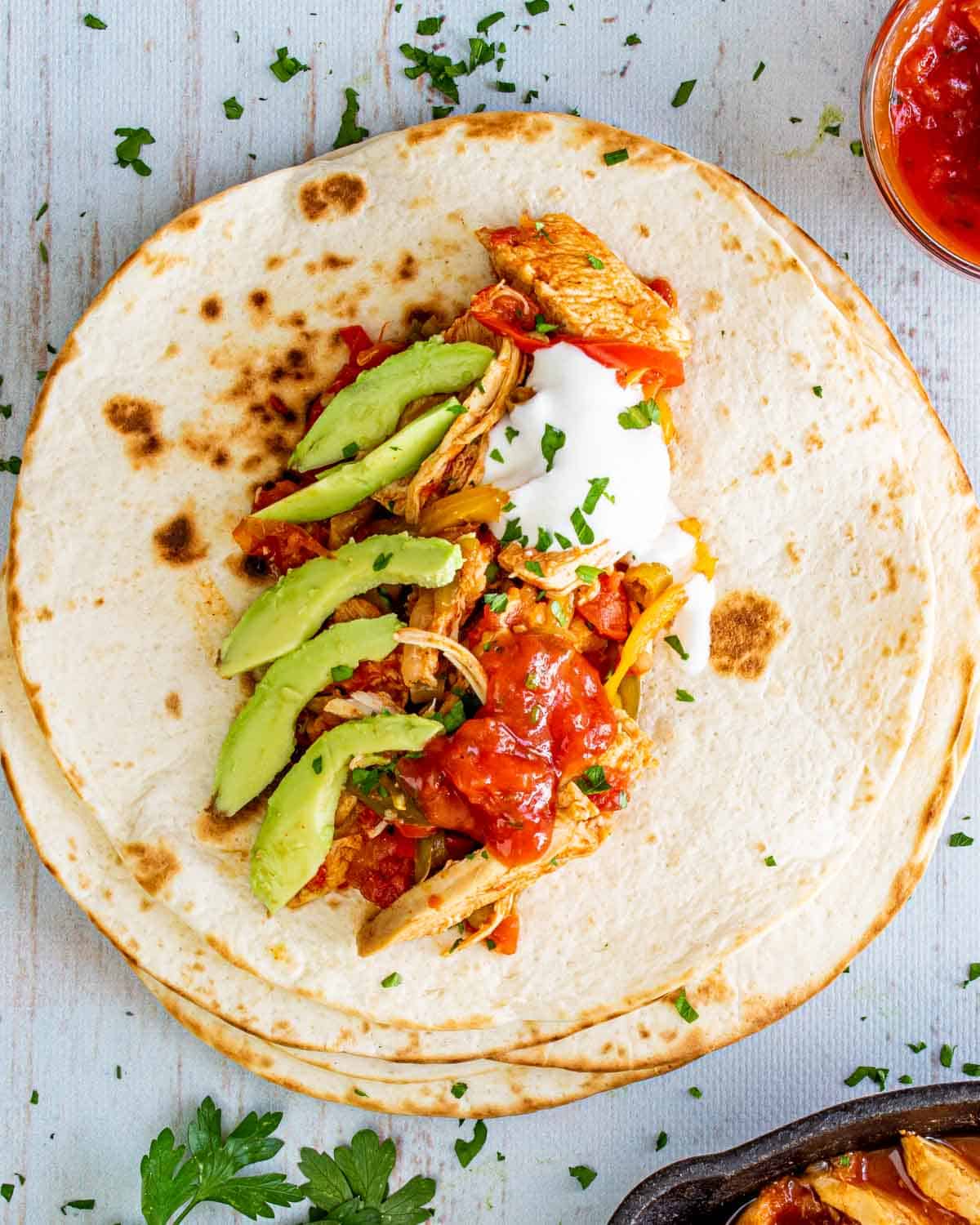 chicken fajitas on a tortilla garnished with sour cream, avocados and limes.
