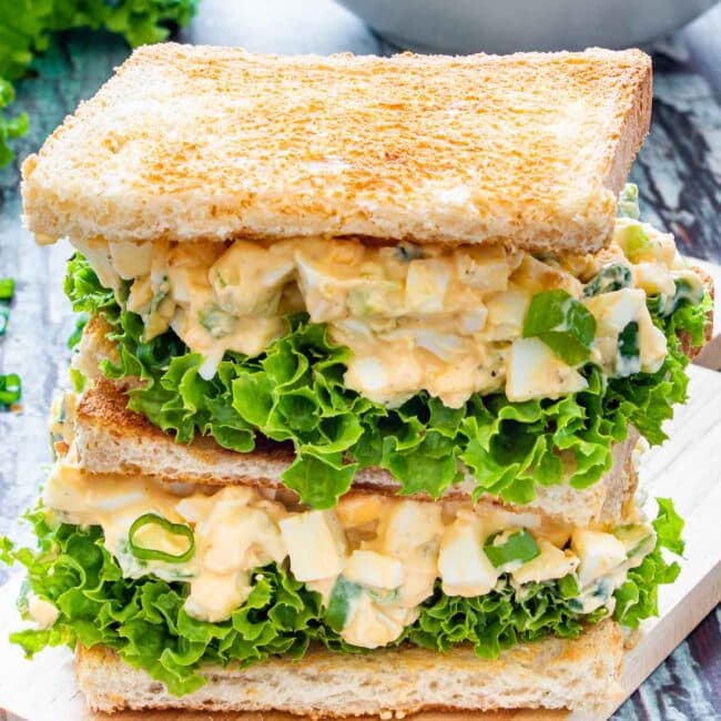 2 egg salad sandwiches on a cutting board.