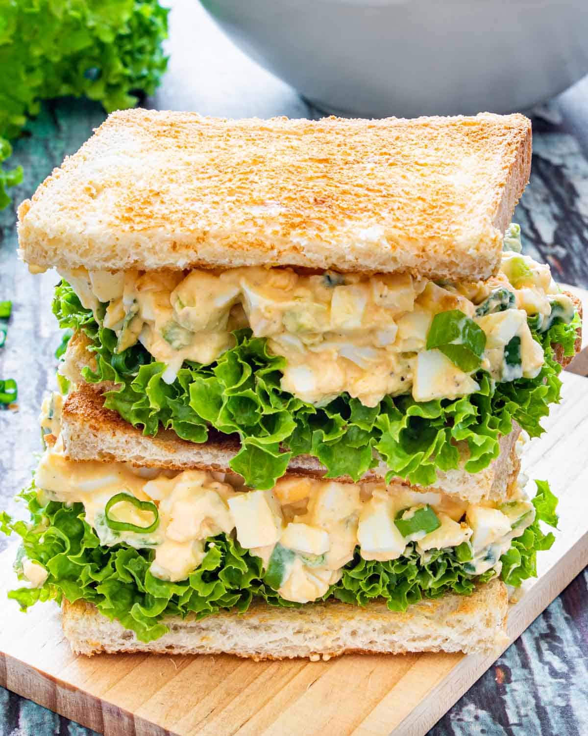 2 egg salad sandwiches on a cutting board.