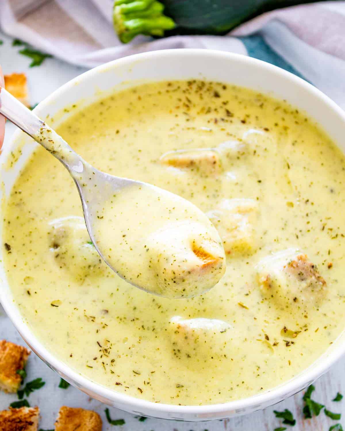 zucchini soup with croutons in a white bowl.
