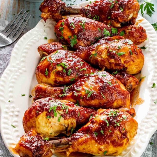 baked bbq chicken drumsticks on a white platter garnished with parsley.