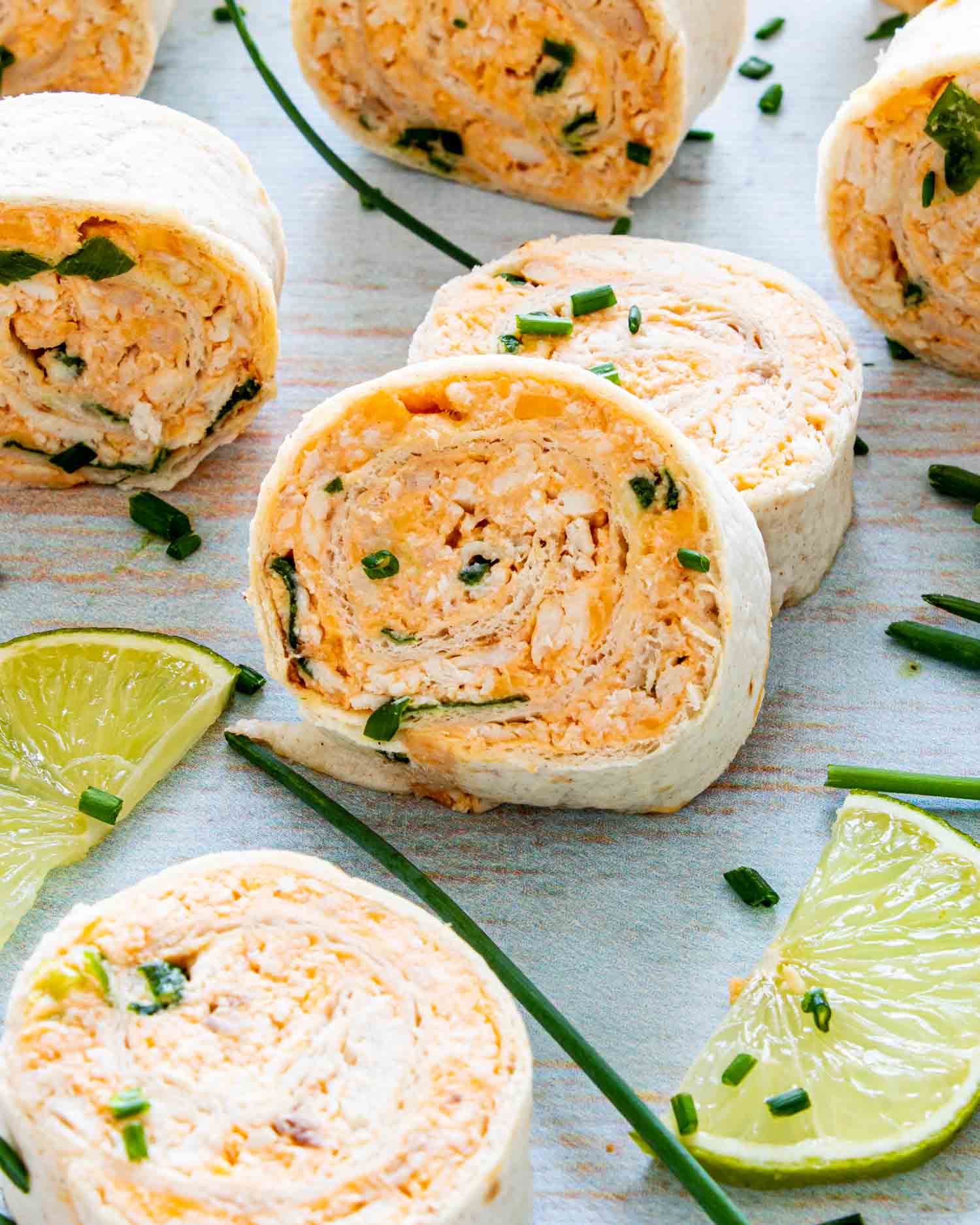 buffalo chicken pinwheels on a platter with lime wedges.