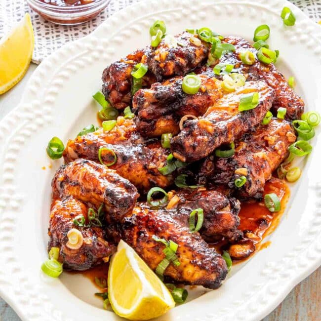 thai chicken wings on a white serving platter garnished with green onions and lemon wedges.