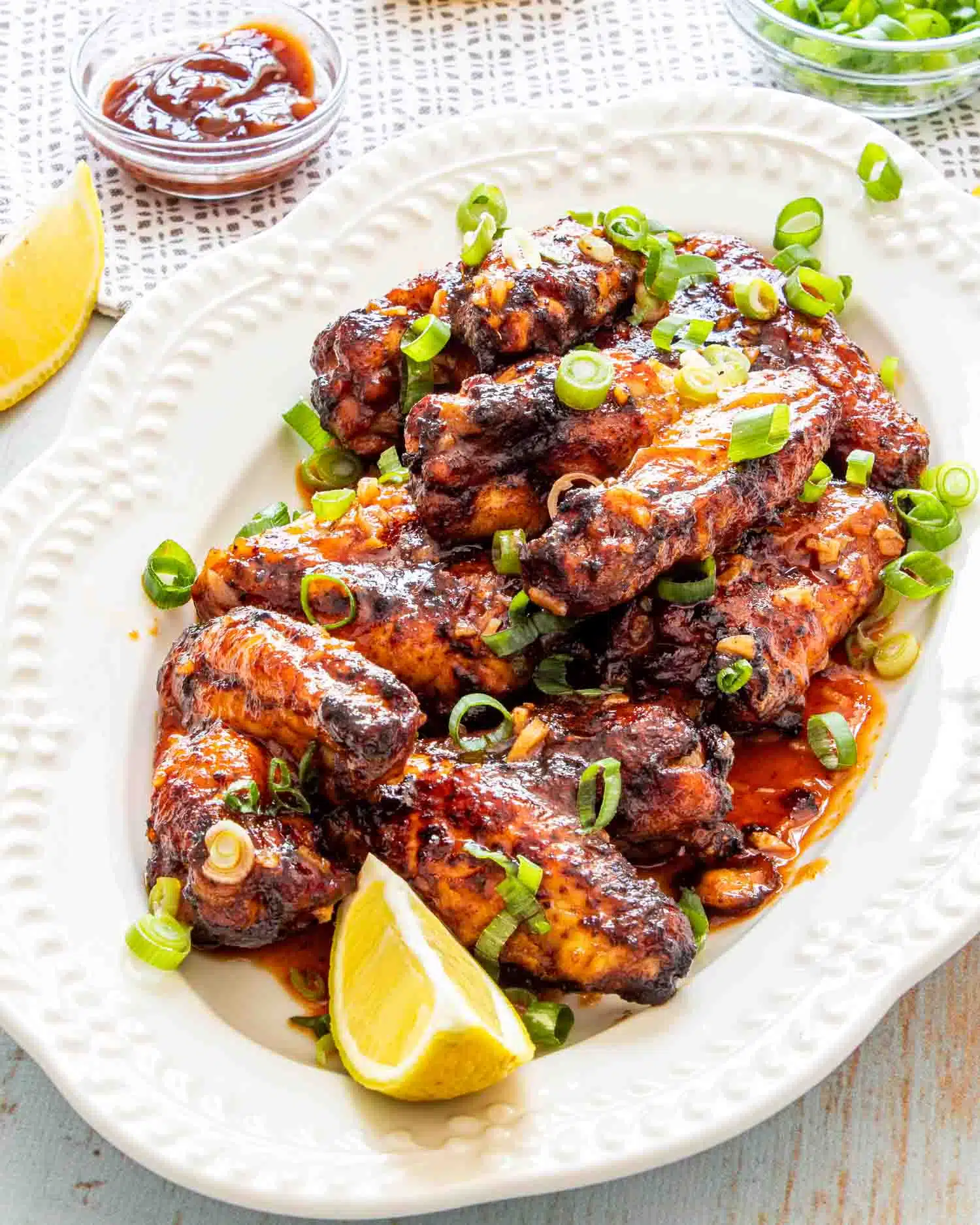 thai chicken wings on a white serving platter garnished with green onions and lemon wedges.