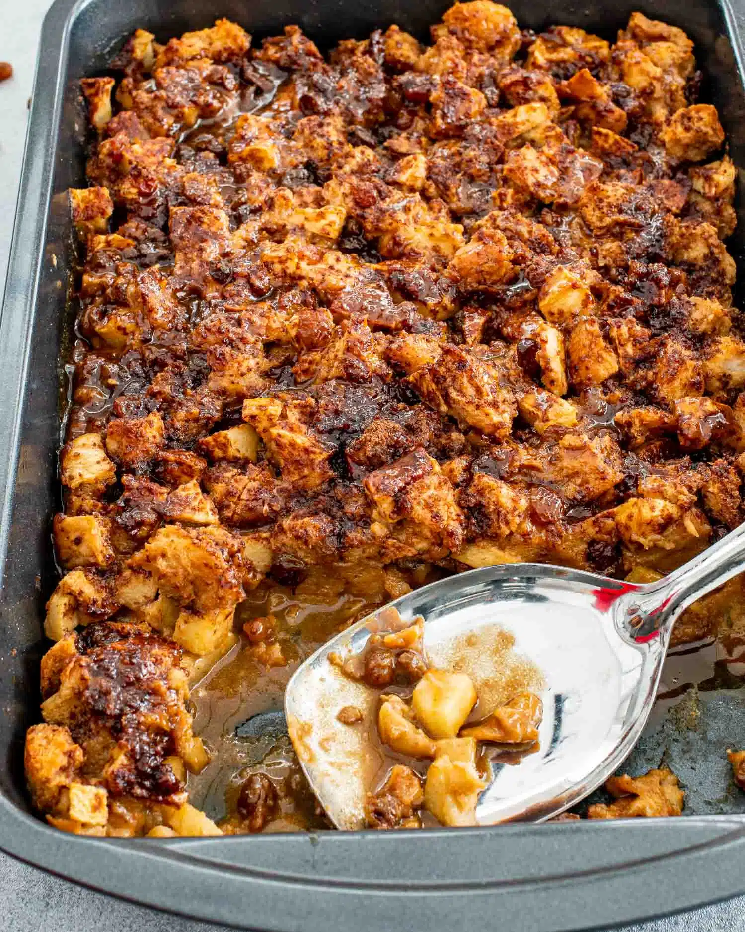 freshly baked apple pie bread pudding in a baking dish with a serving spoon.