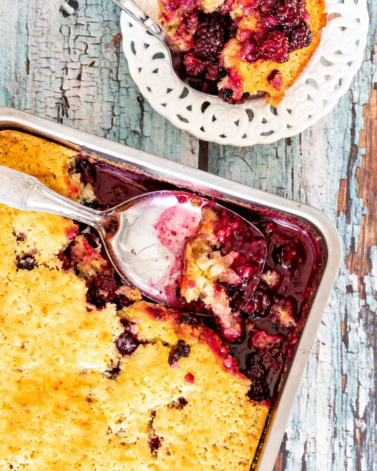 freshly baked blackberry cobbler in a baking pan with a couple servings missing and a serving spoon inside.