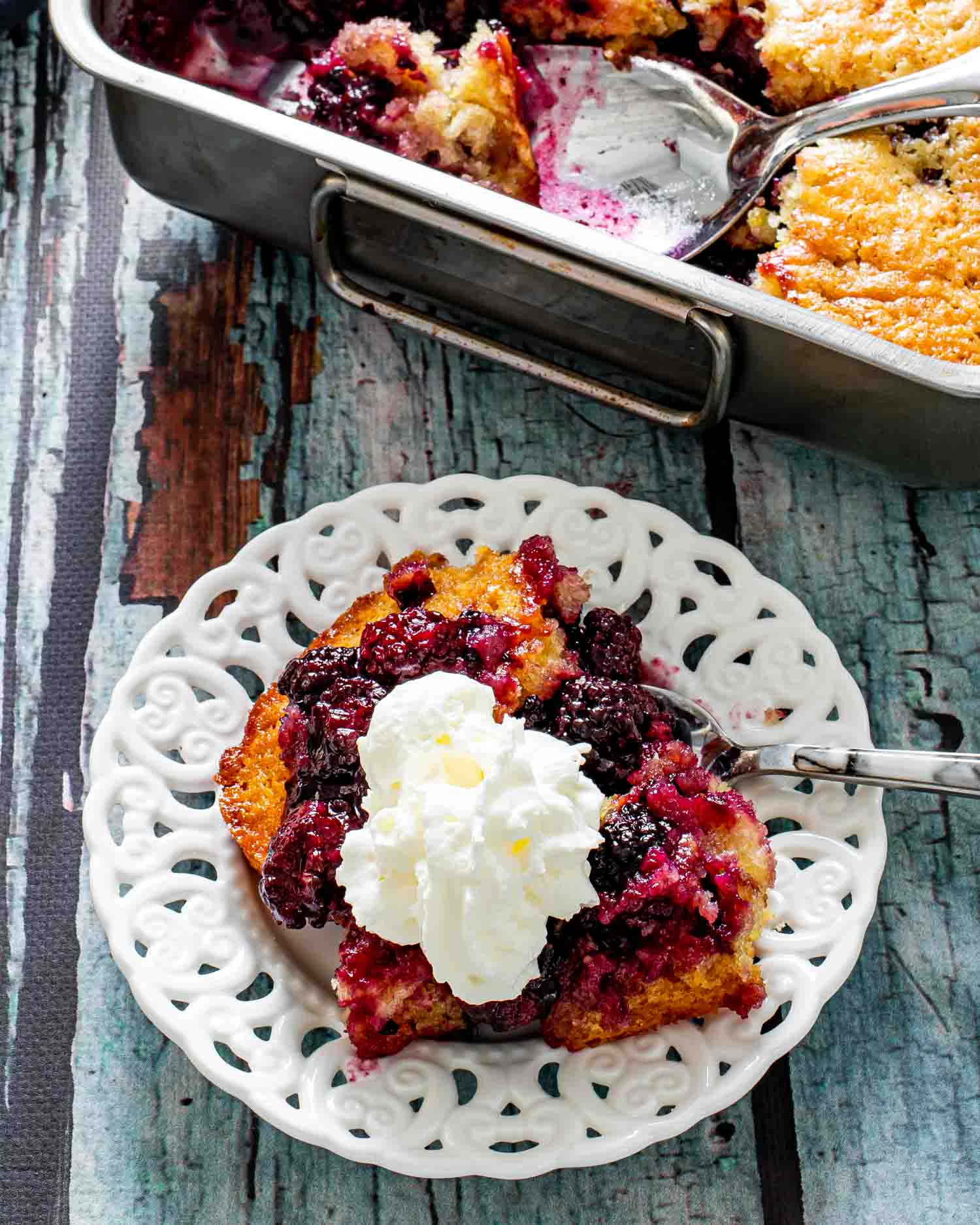a serving of blackberry cobbler with whipped cream on a white plate.