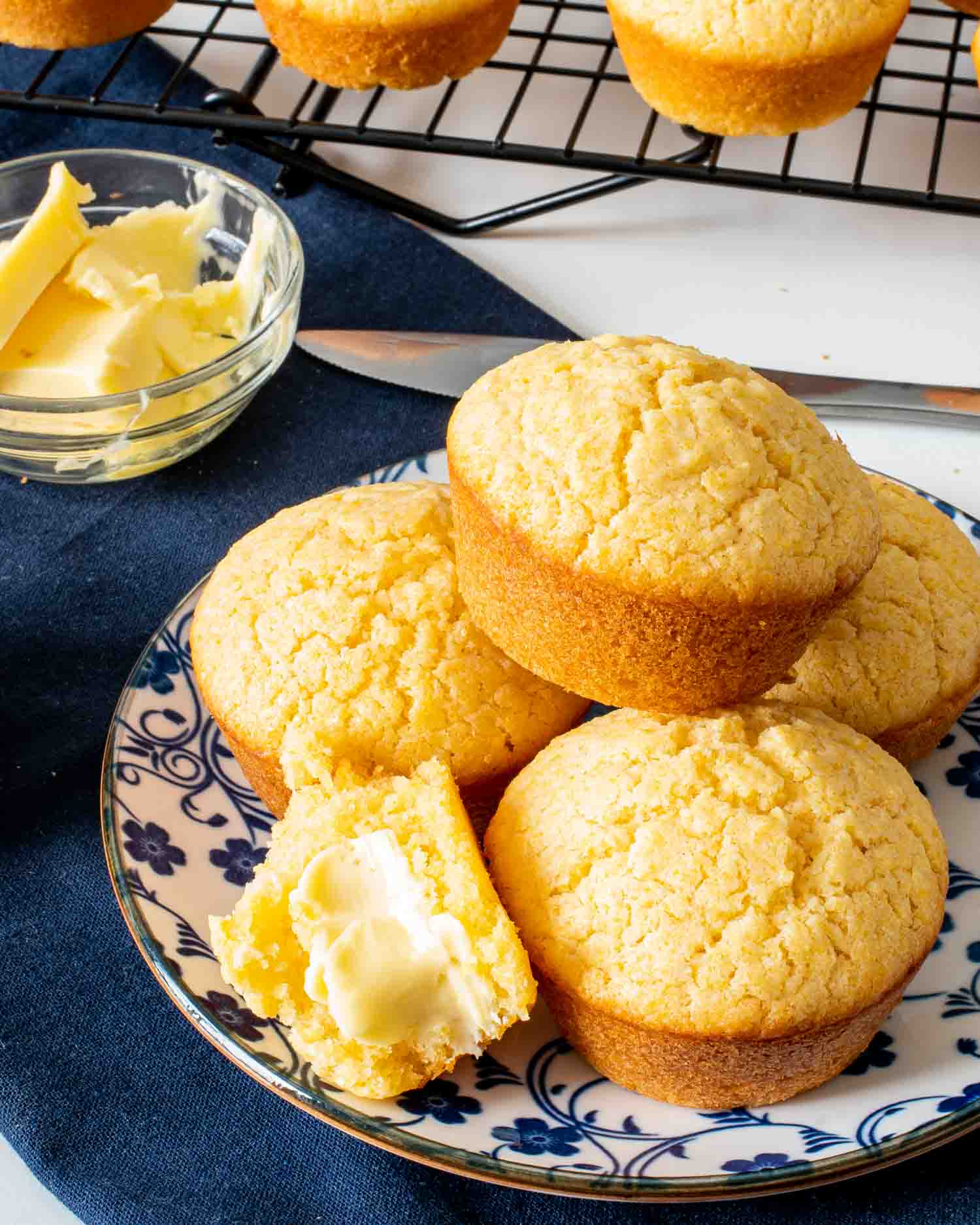 a cornbread muffin broken in half with butter on a plate with a few other cornbread muffins.