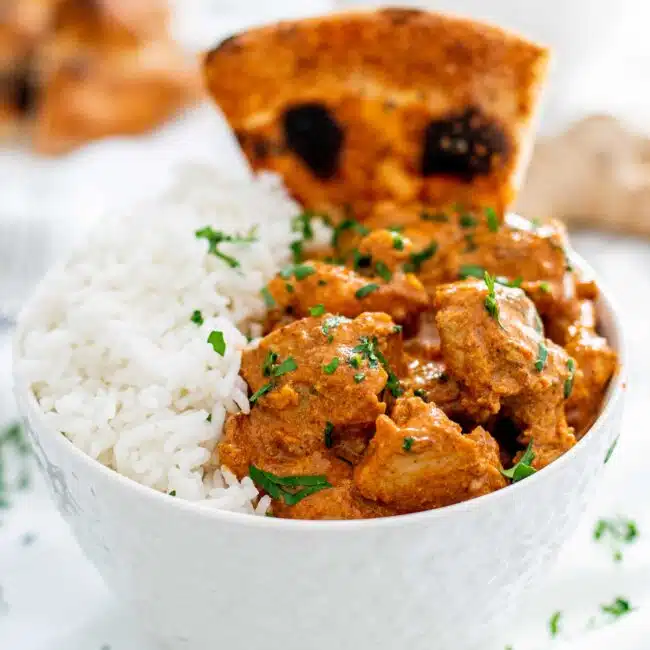 chicken tikka masala with rice in a white bowl and a piece of naan.