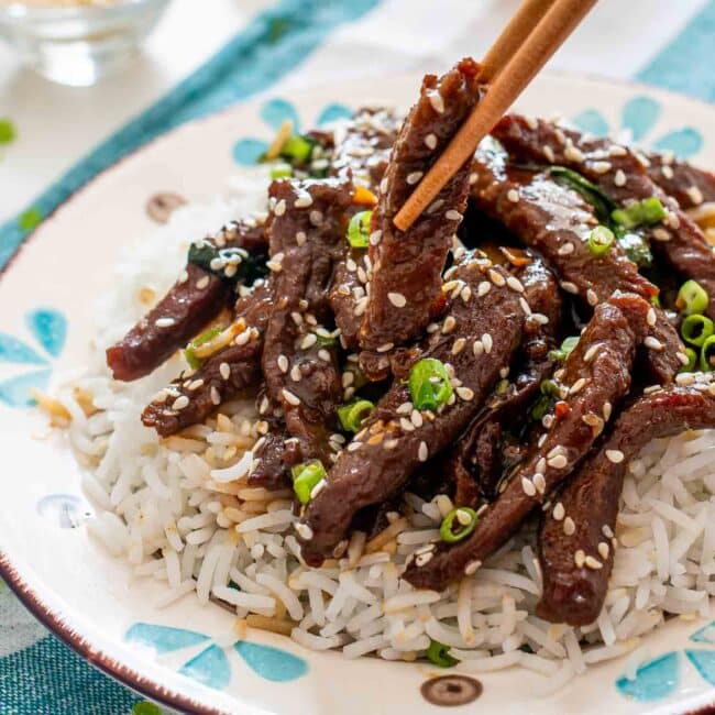 chinese sizzling beef on a bed of rice in a plate.