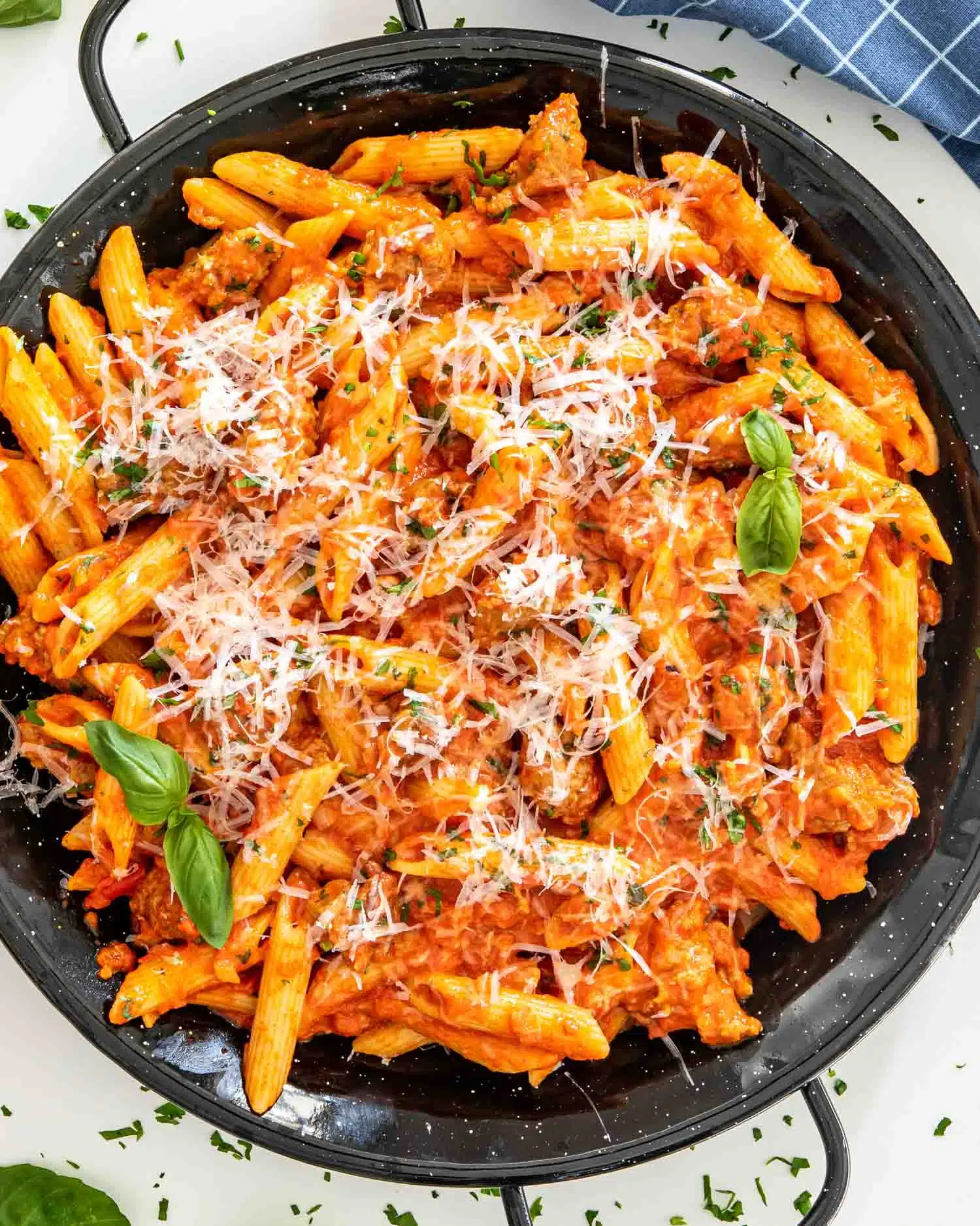 creamy red pepper sausage pasta in a black skillet garnished with parmesan cheese.