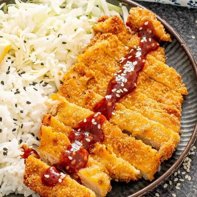 sliced up chicken katsu on a plate with rice and tonkatsu sauce.