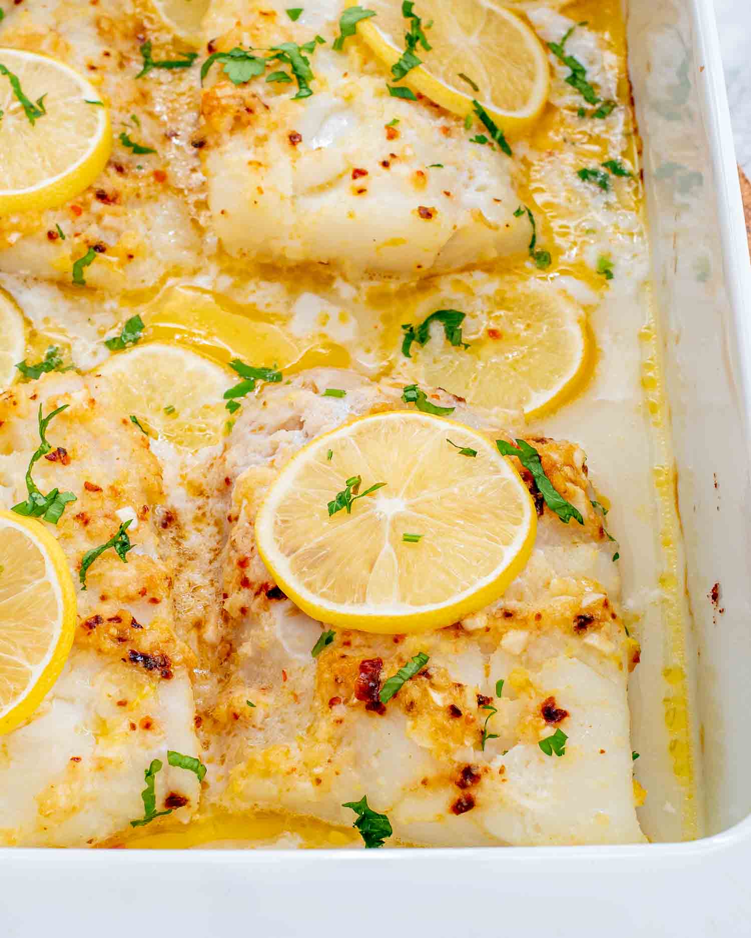 freshly baked lemon butter cod in a white baking pan.