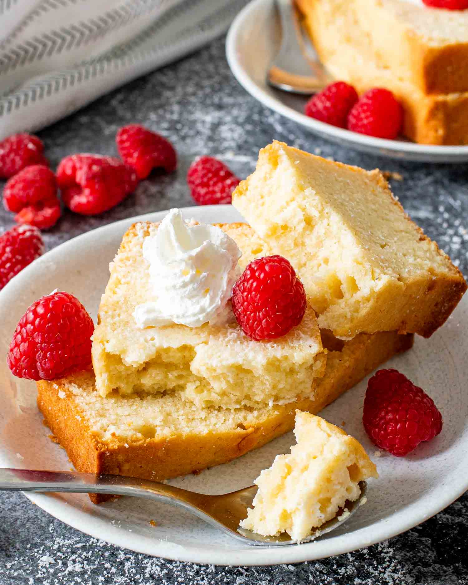 a couple slices of condensed milk pound cake on a dessert plate garnished with raspberries.