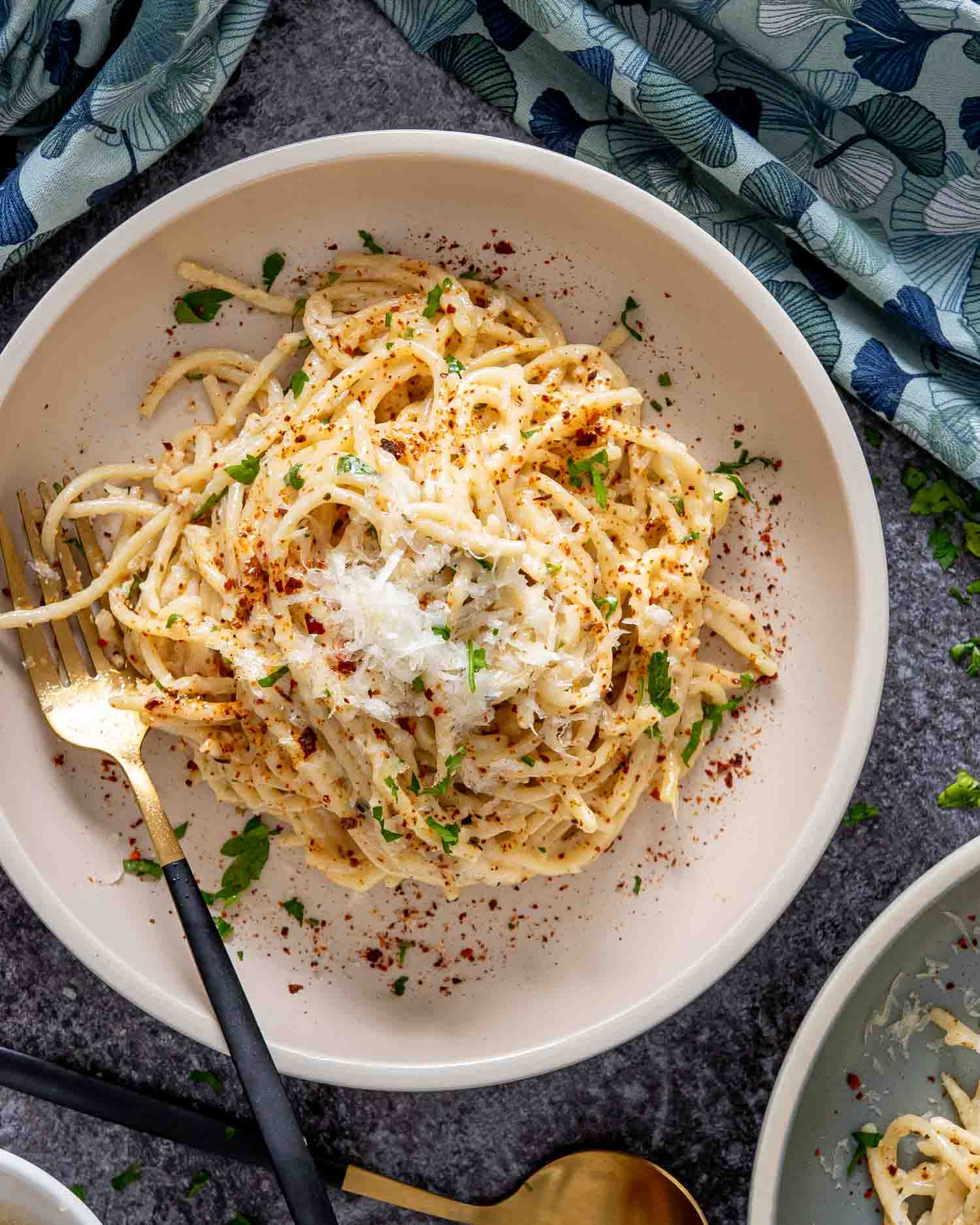 garlic butter spaghetti in a white bowl garnished with parsley and red pepper flakes.