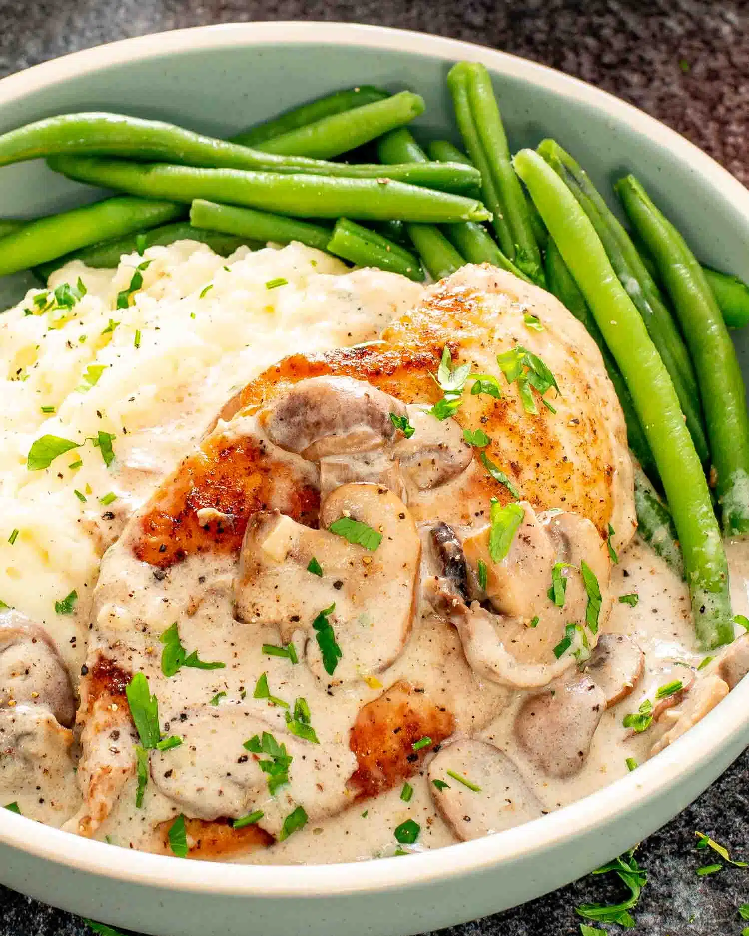 a piece of creamy garlic mushroom chicken in a blue bowl with mashed potatoes.