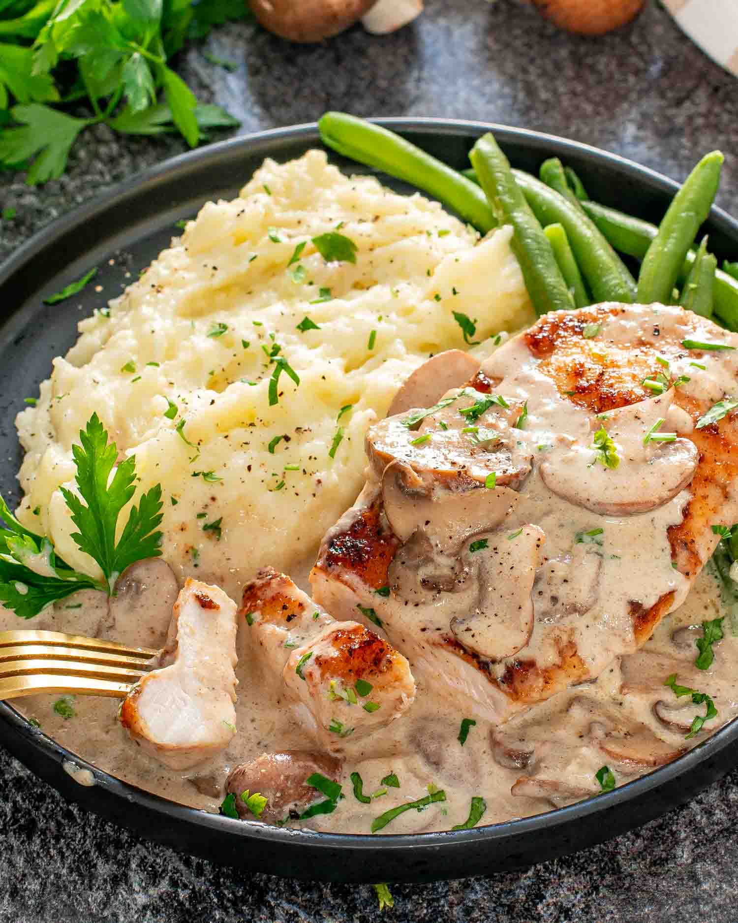 a piece of creamy garlic mushroom chicken on a black plate with mashed potatoes.
