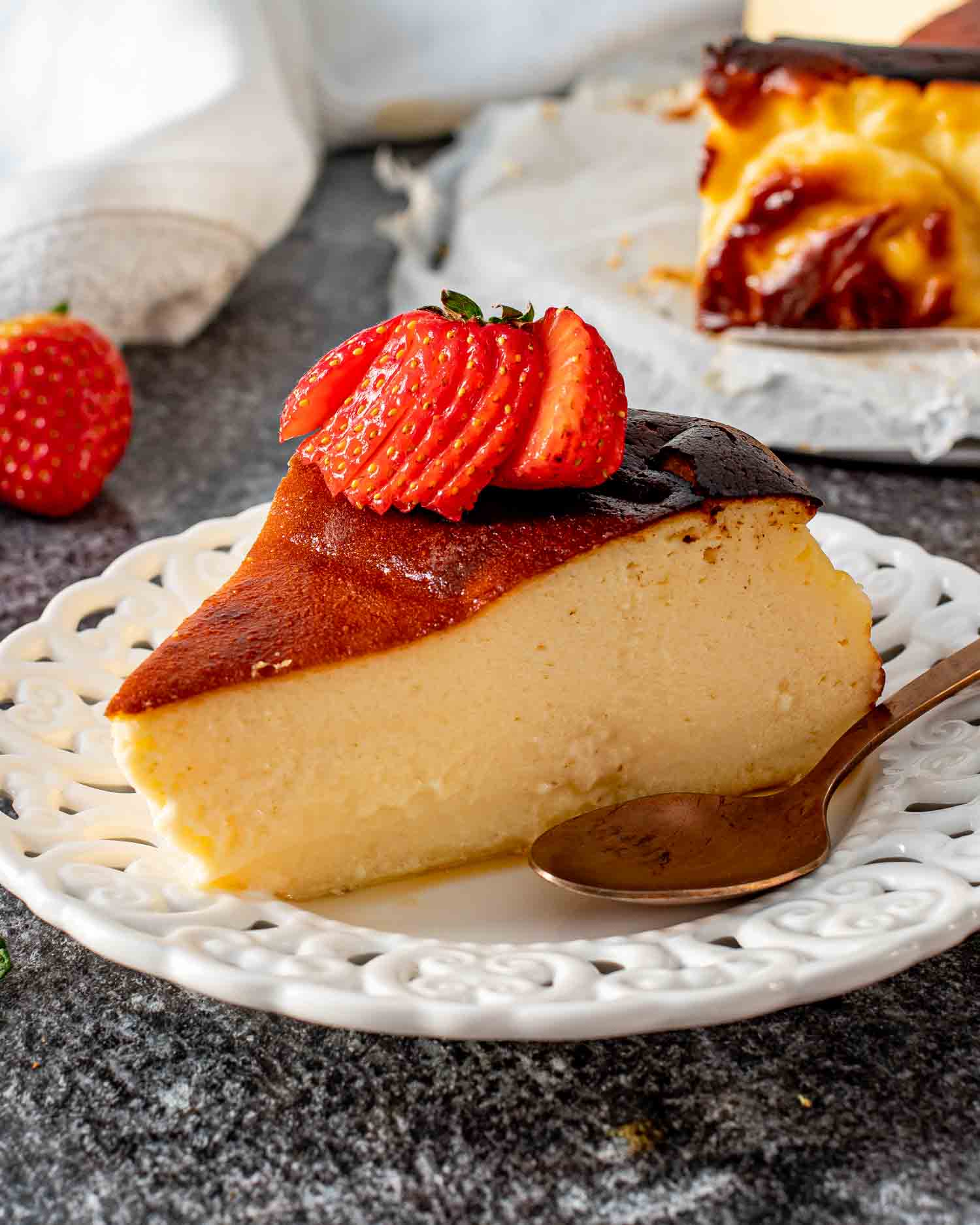 a slice of burnt basque cheesecake on a white plate topped with a strawberry.