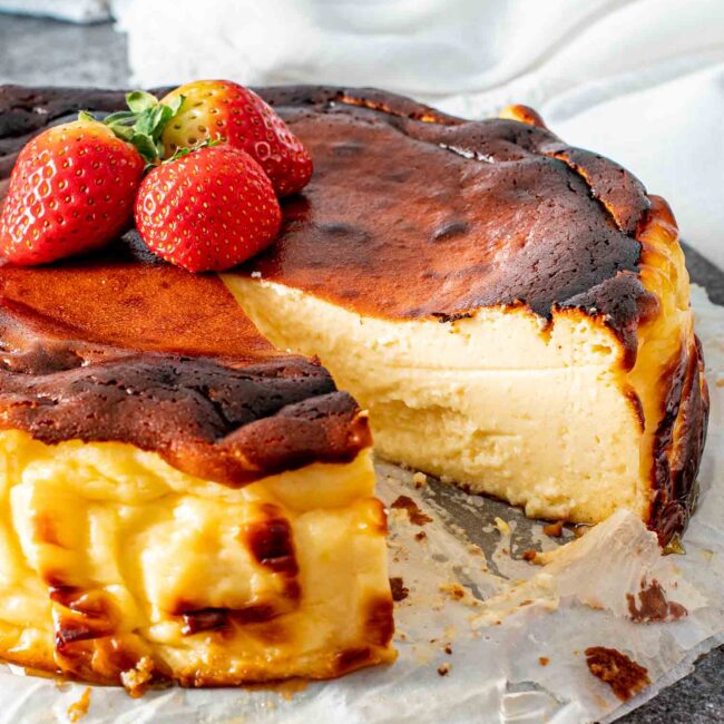 a basque cheesecake with a slice missing and topped with strawberries.