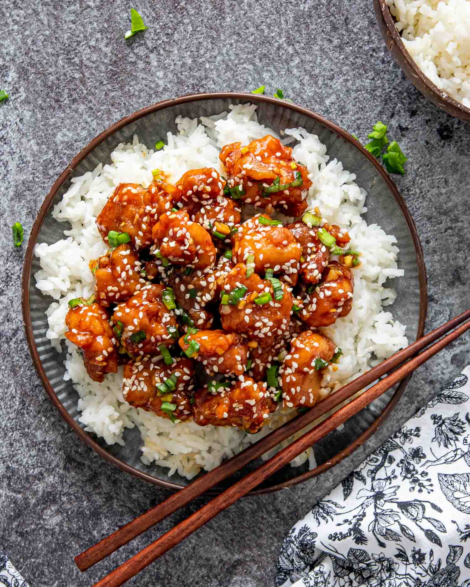 general tso's chicken over a bed of rice in a plate with chop sticks.