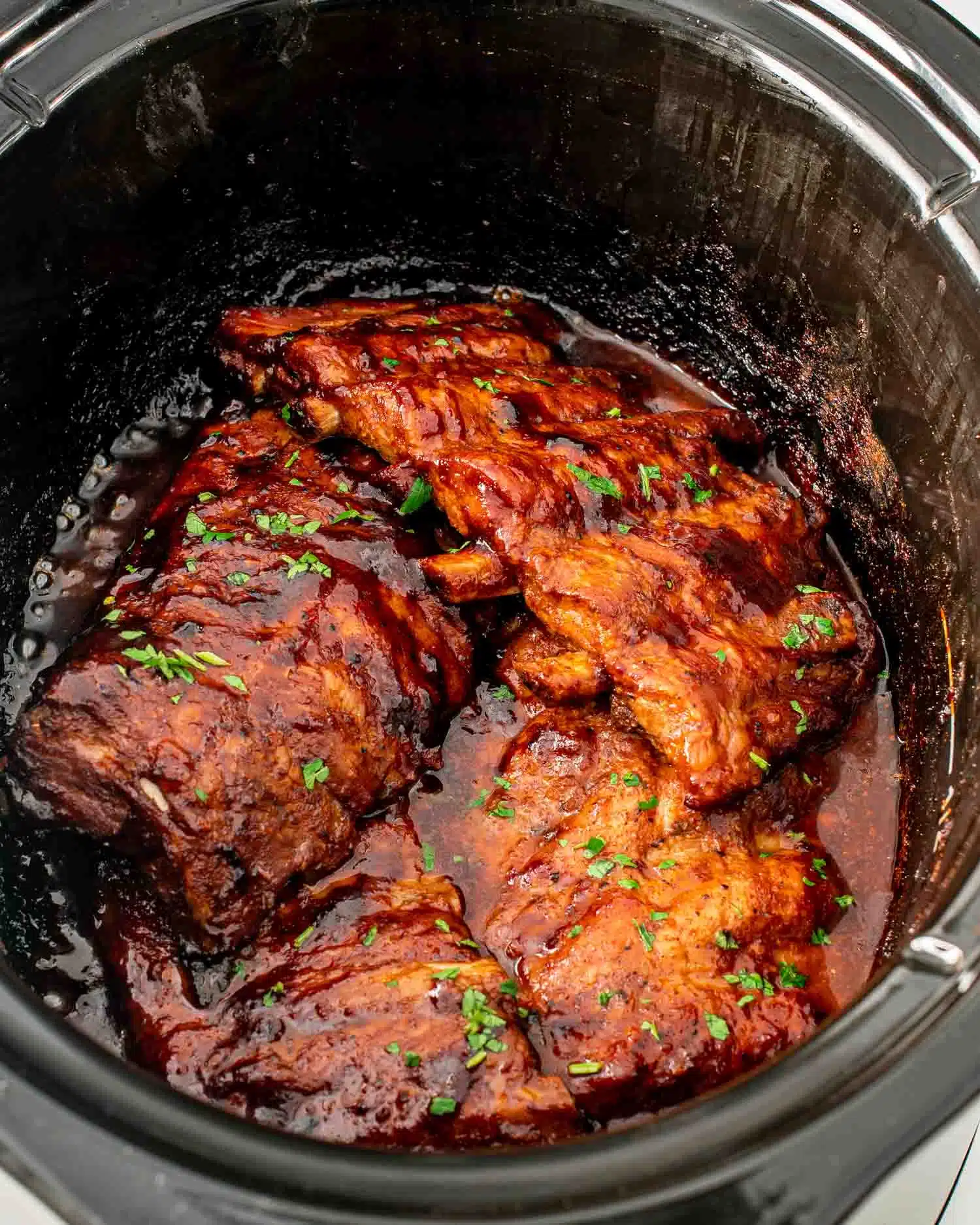 freshly made slow cooker ribs right in the slow cooker with bbq sauce and garnished with parsley.