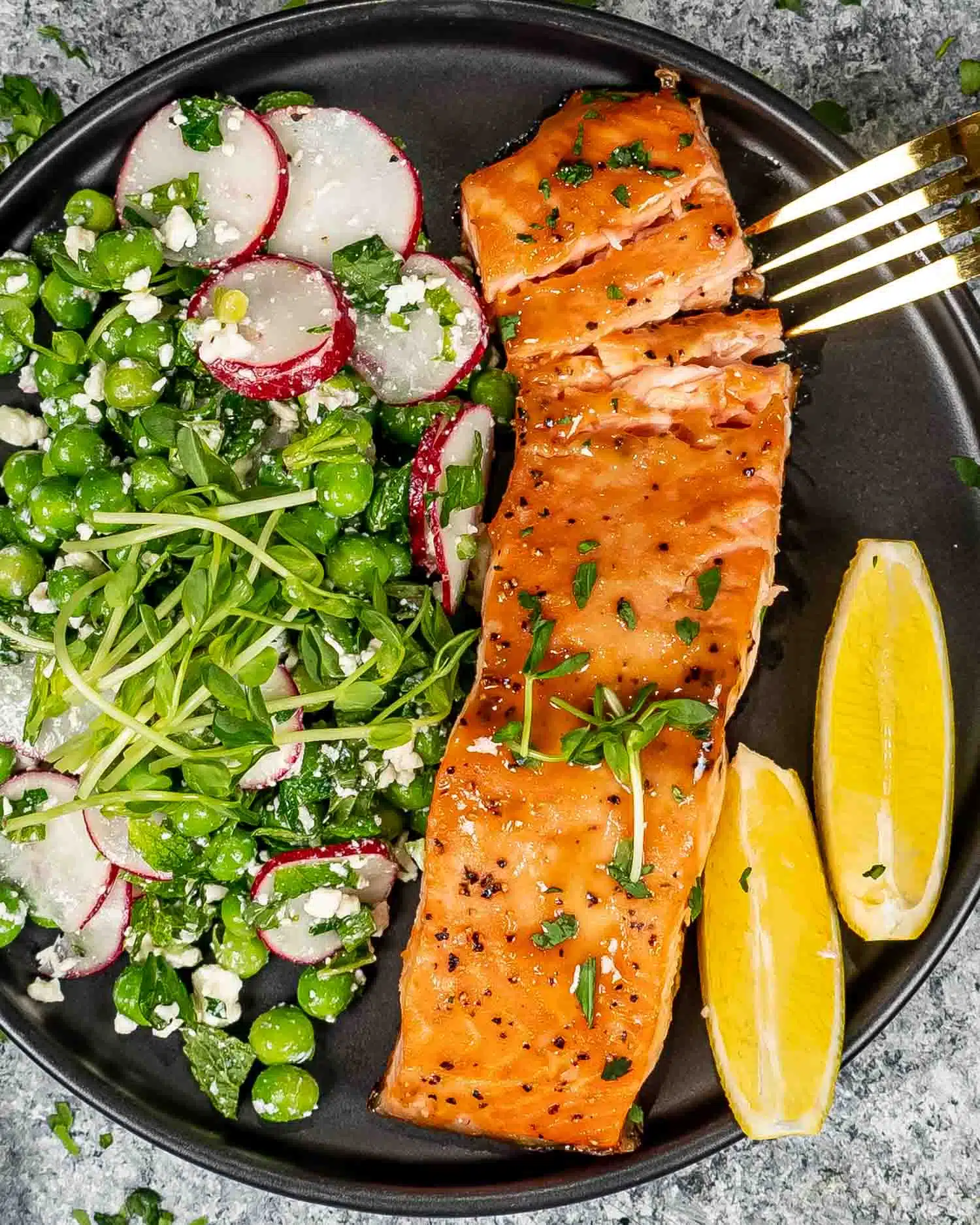 baked salmon with mustard glaze on a black plate with pea salad.