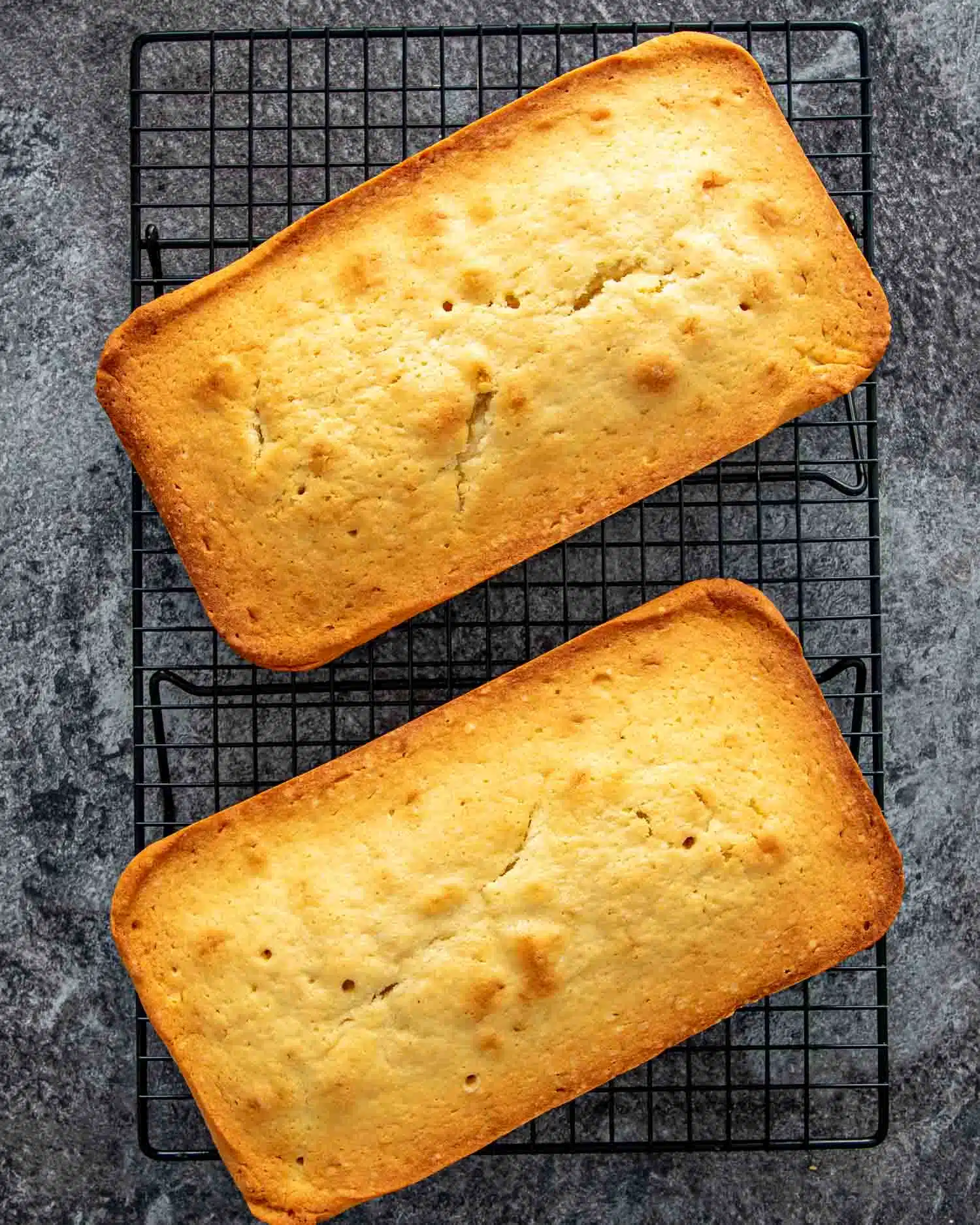 2 condensed milk pound cakes on a black cooling rack.