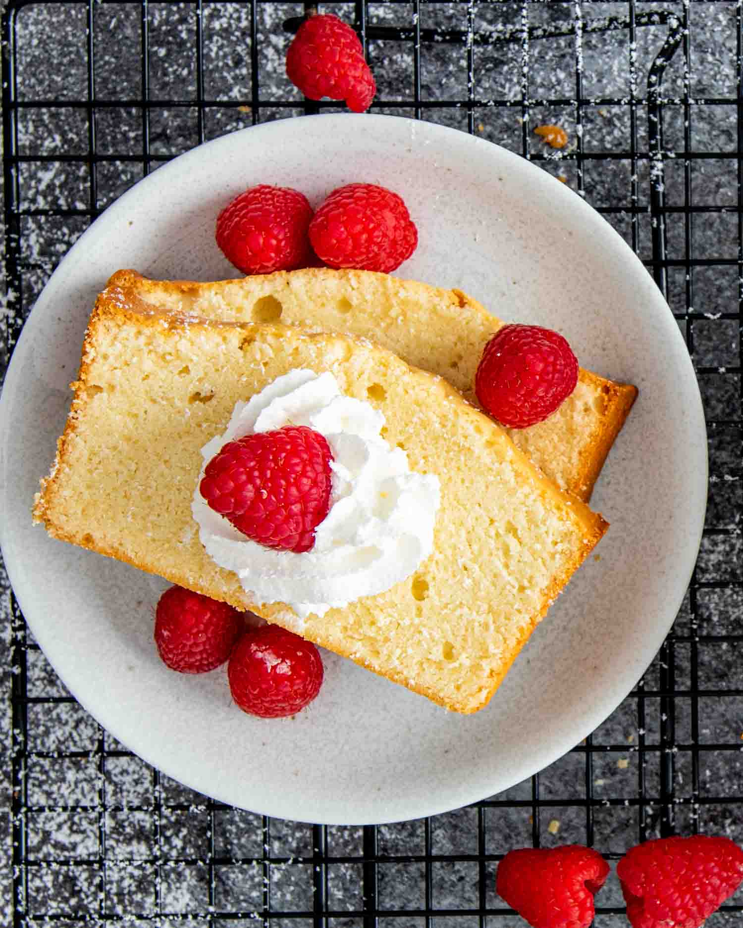 a couple slices of condensed milk pound cake on a dessert plate garnished with raspberries.