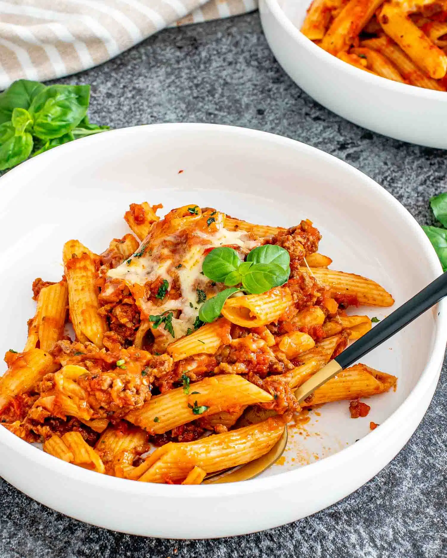 a serving of baked mostaccioli in a white bowl garnished with a bit of fresh basil.