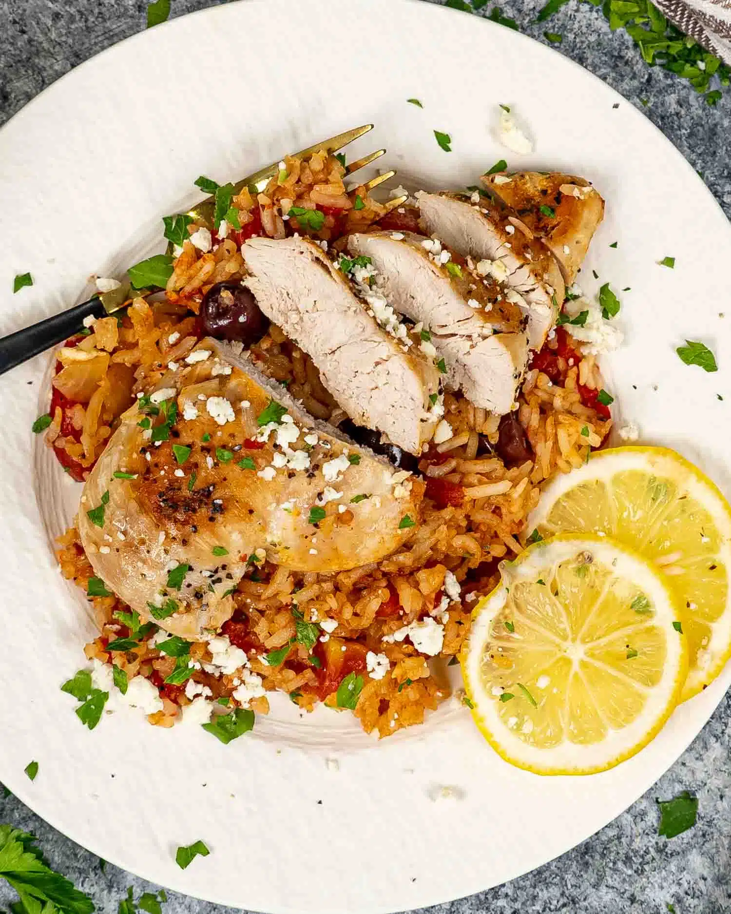 a serving of mediterranean chicken and rice on a white plate garnished with feta cheese and lemon slices.