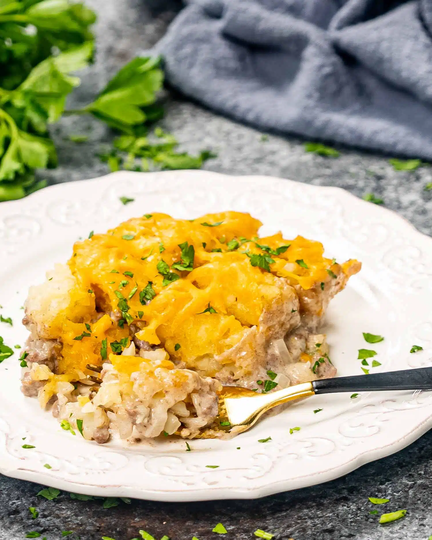 a serving of tater tot casserole on a white dish with a fork and garnished with parsley.