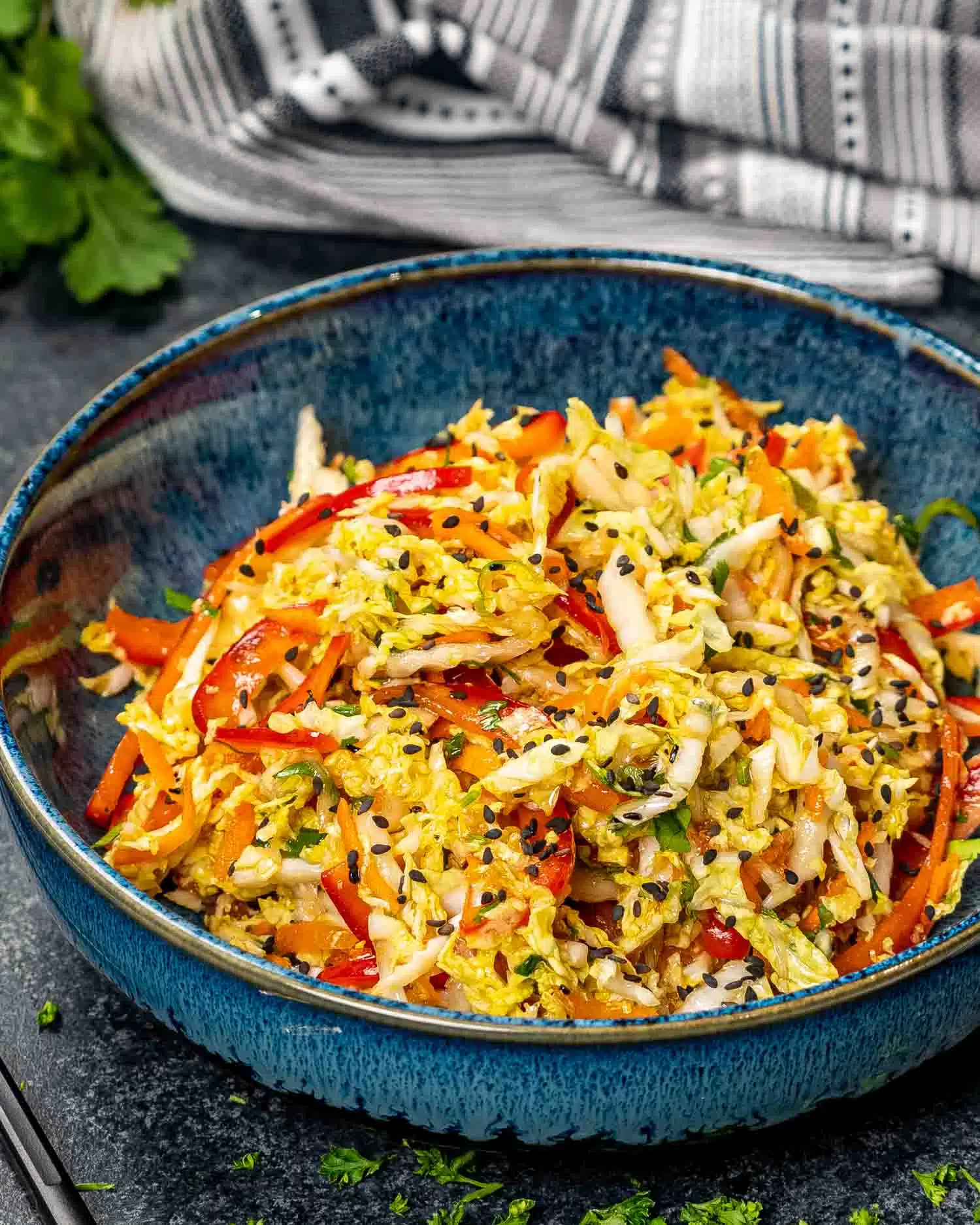 asian style slaw in a blue bowl garnished with sesame seeds.