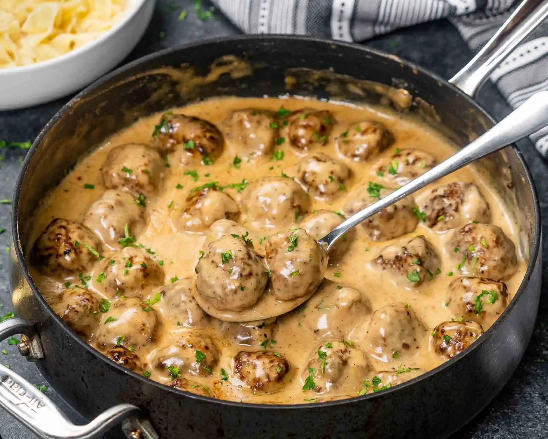 swedish meatballs with lots of sauce in a skillet, freshly made and garnished with parsley.