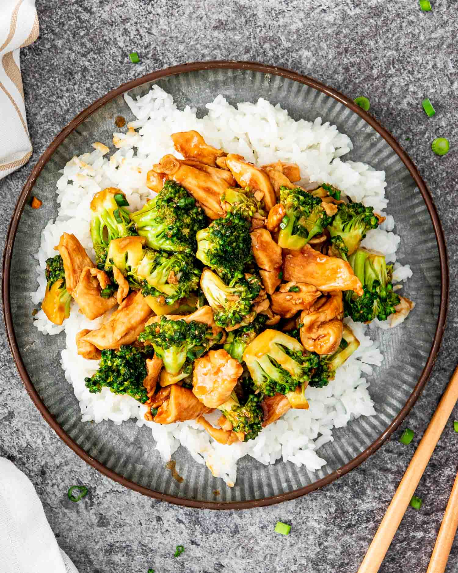 asian style chicken and broccoli over a bed of rice on a metal plate.