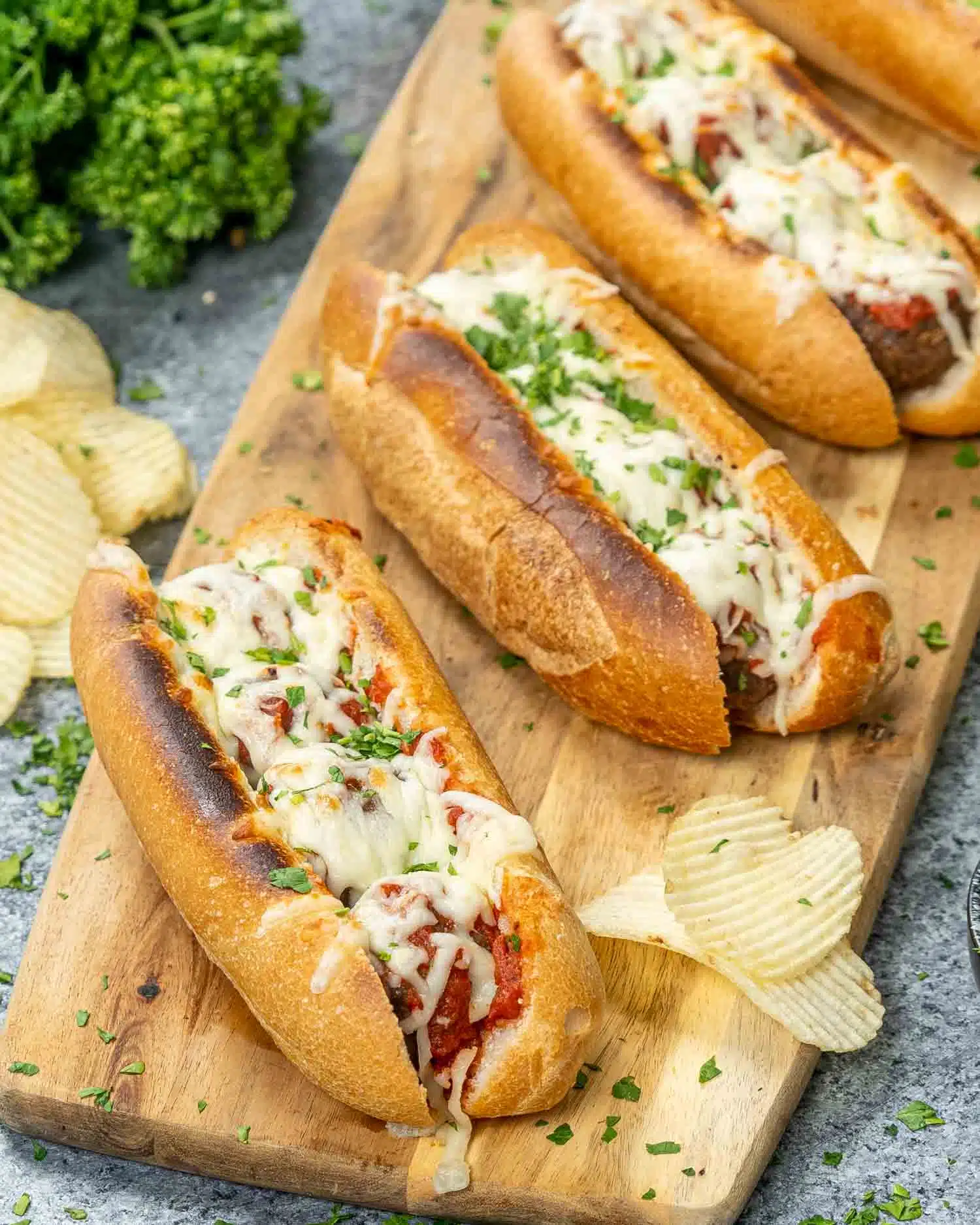 4 meatball subs on a cutting board with potato chips.