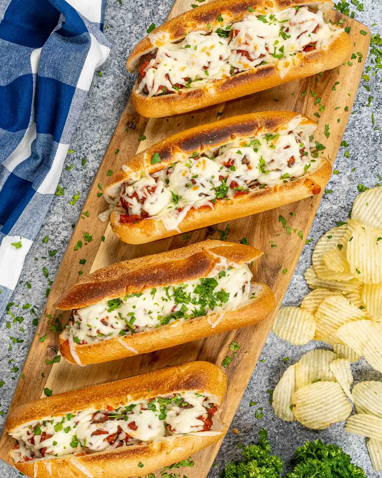 4 meatball subs on a cutting board with potato chips.
