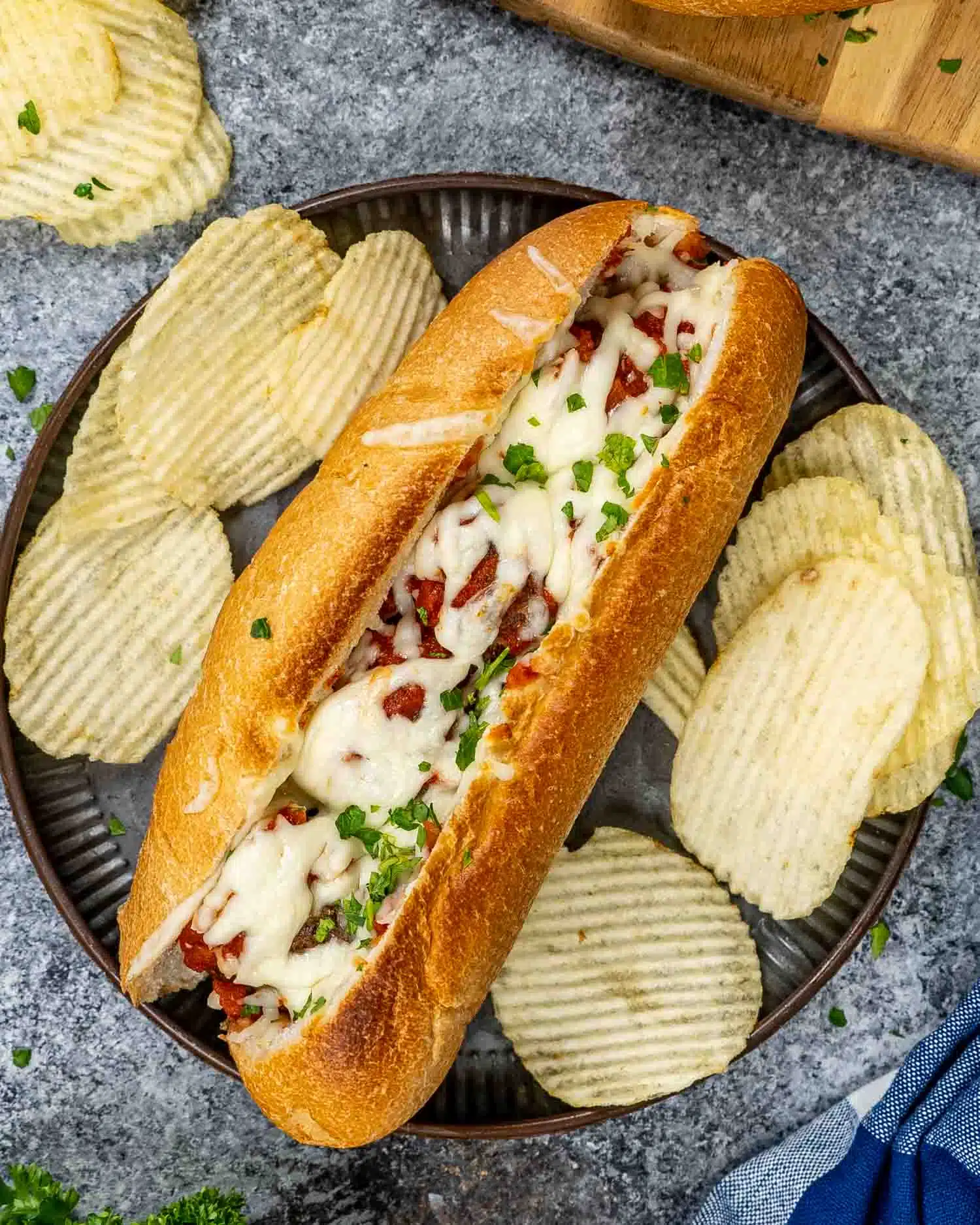 a meatball sub garnished with parsley with potato chips on a plate.