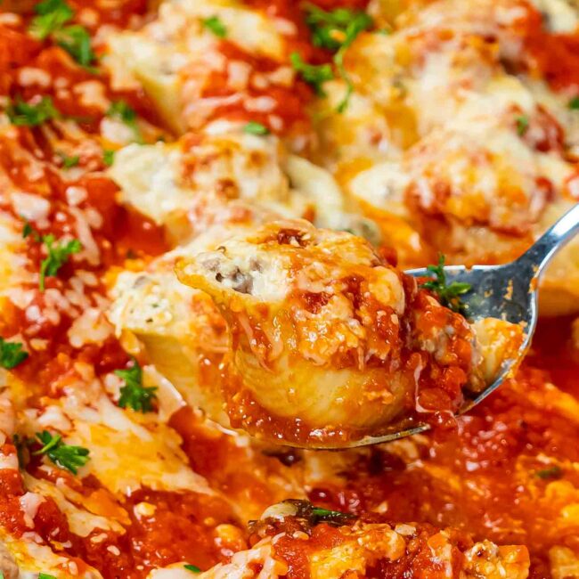 freshly baked stuffed shells in a white casserole dish garnished with some parsley.