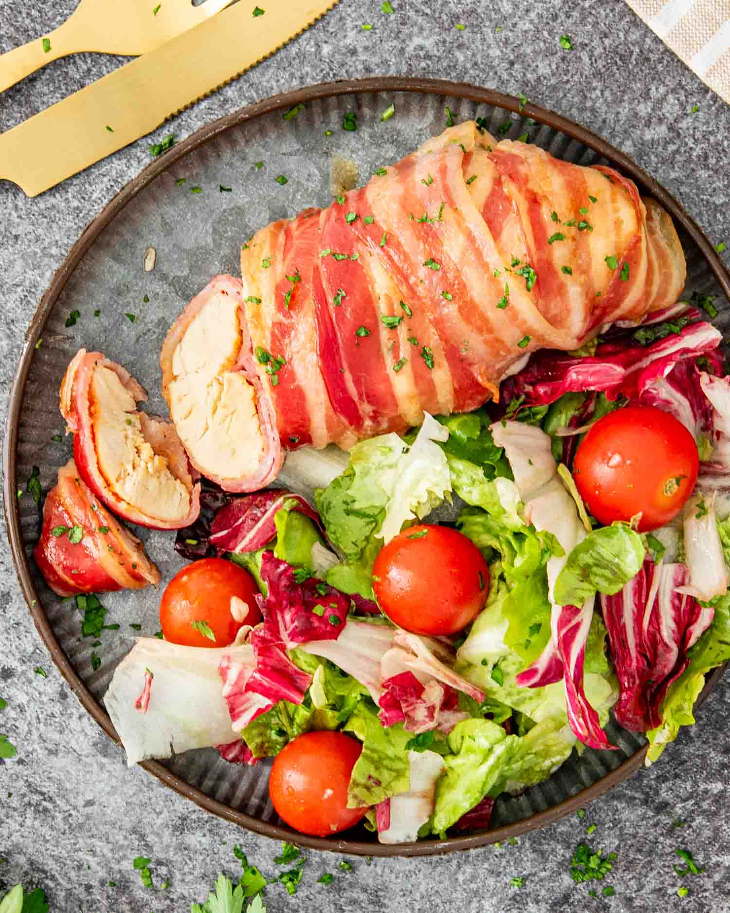 a bacon wrapped chicken breast on a plate along a tossed salad.