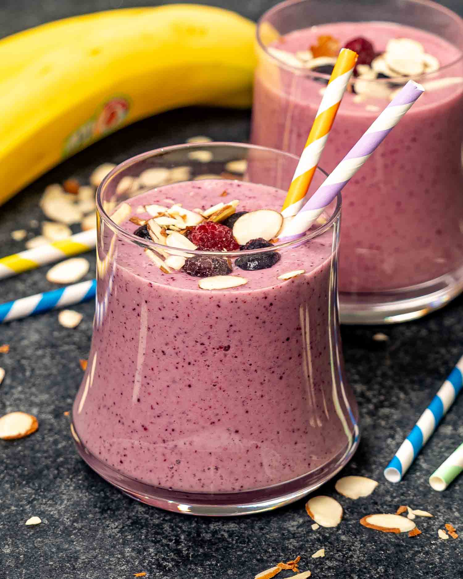 a berry and banana breakfast smoothie in a glass garnished with sliced almonds with two straws inside.
