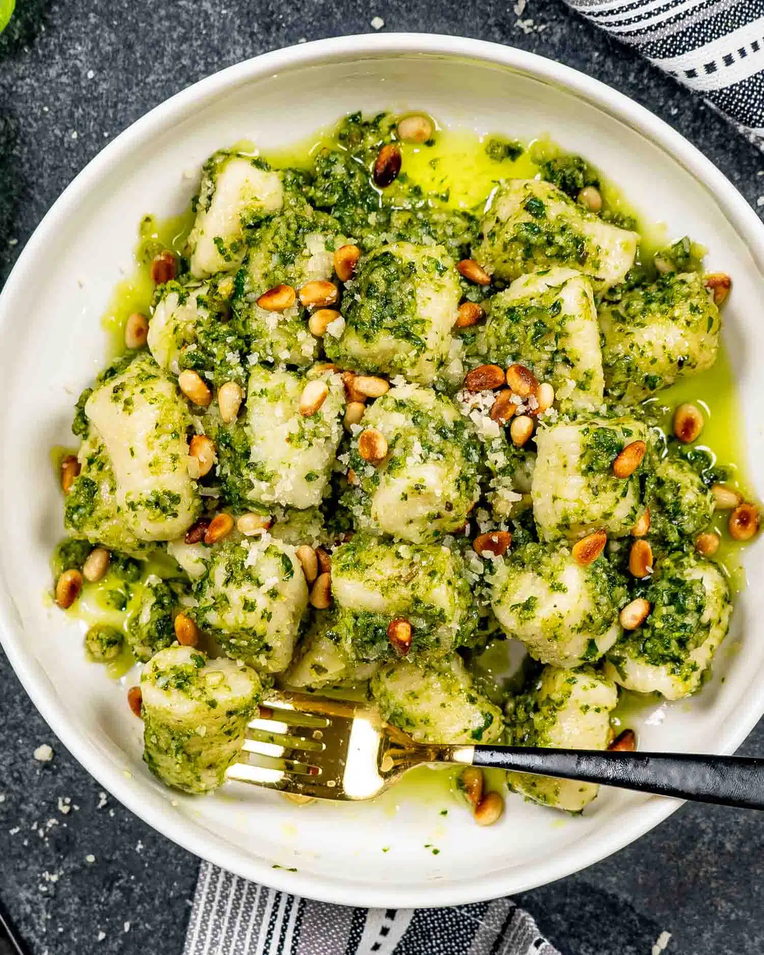a white bowl loaded with pesto gnocchi that's topped with toasted pine nuts.