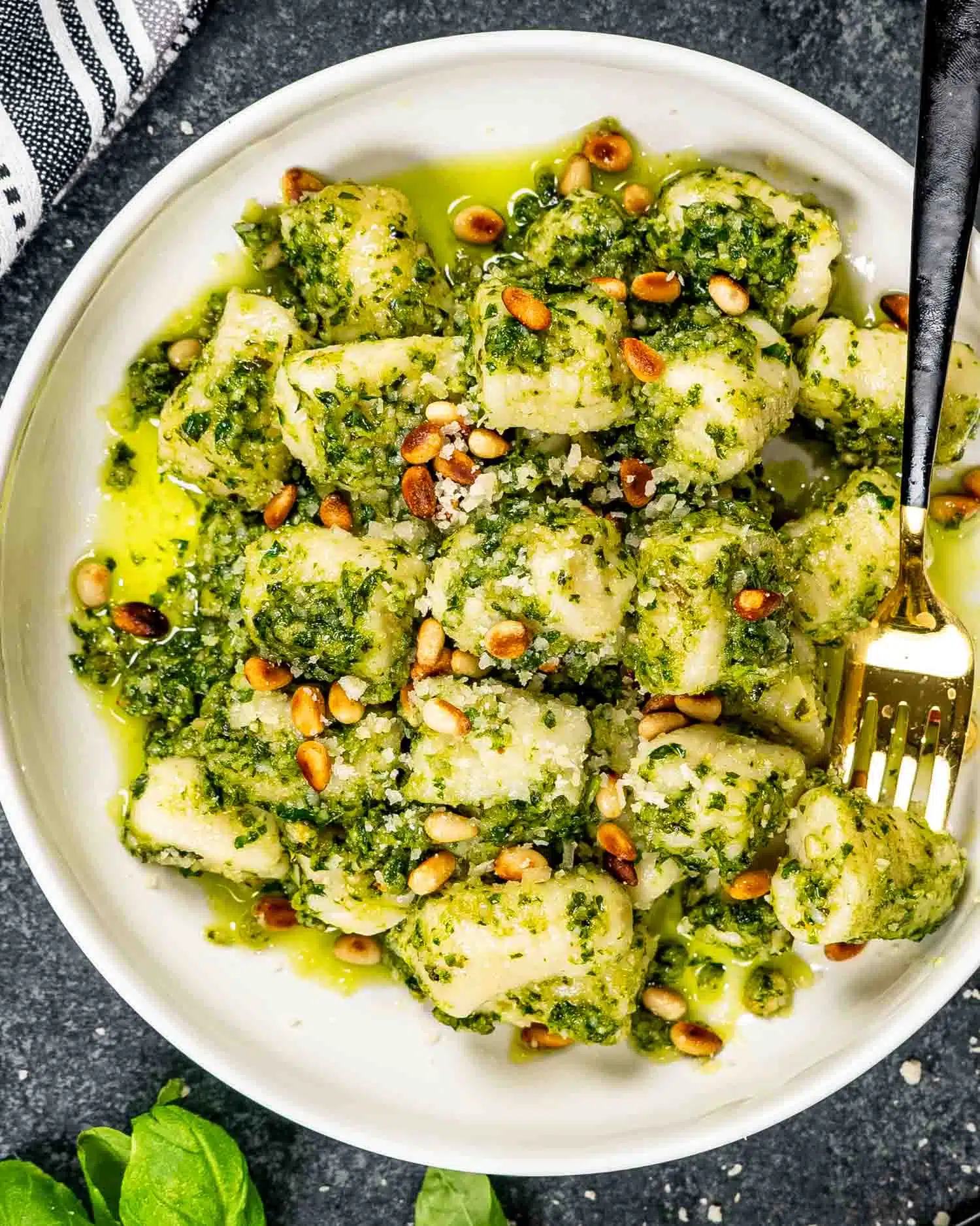 a serving of pesto gnocchi with toasted pine nuts in a white bowl.