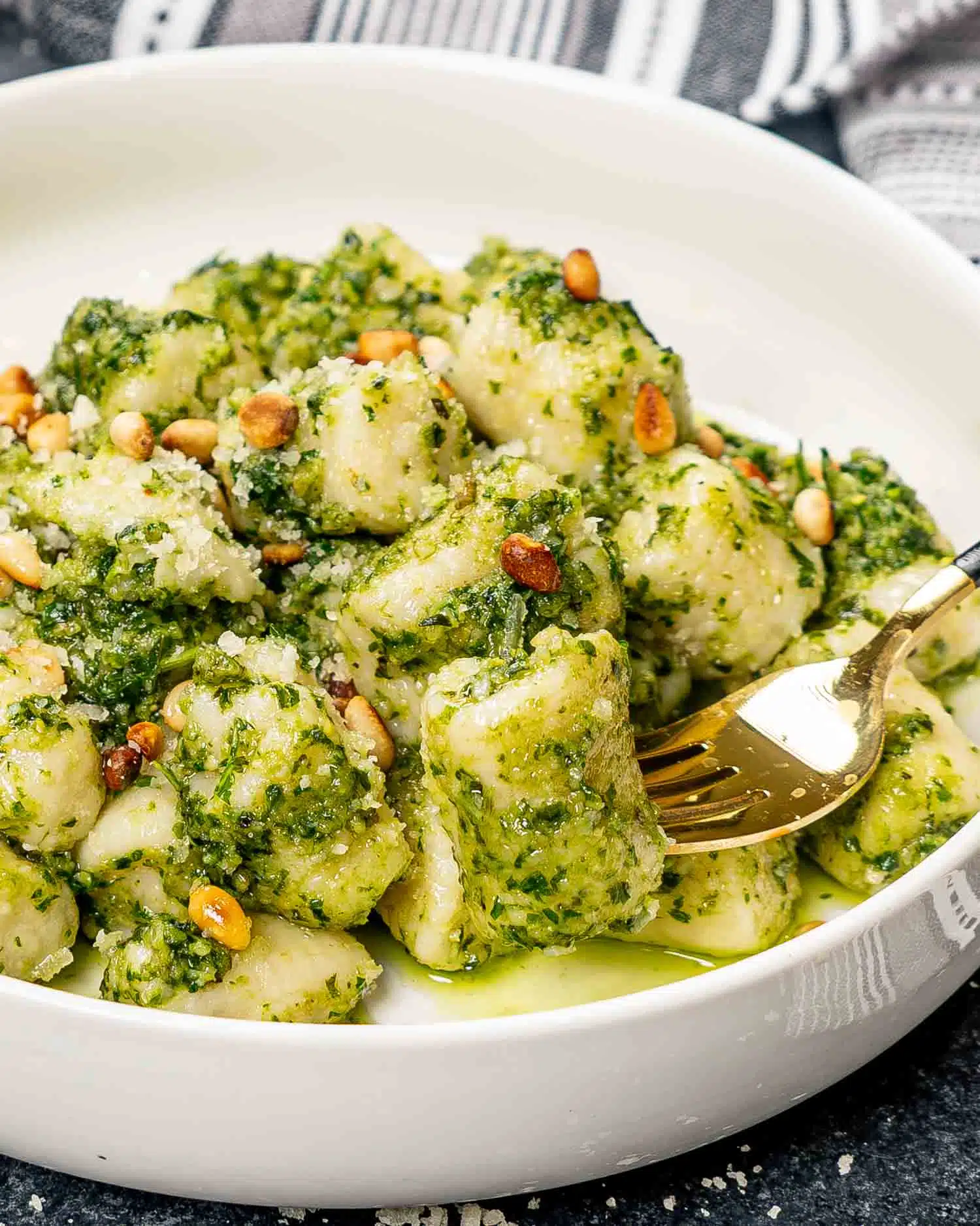 a serving of pesto gnocchi with toasted pine nuts in a white bowl.
